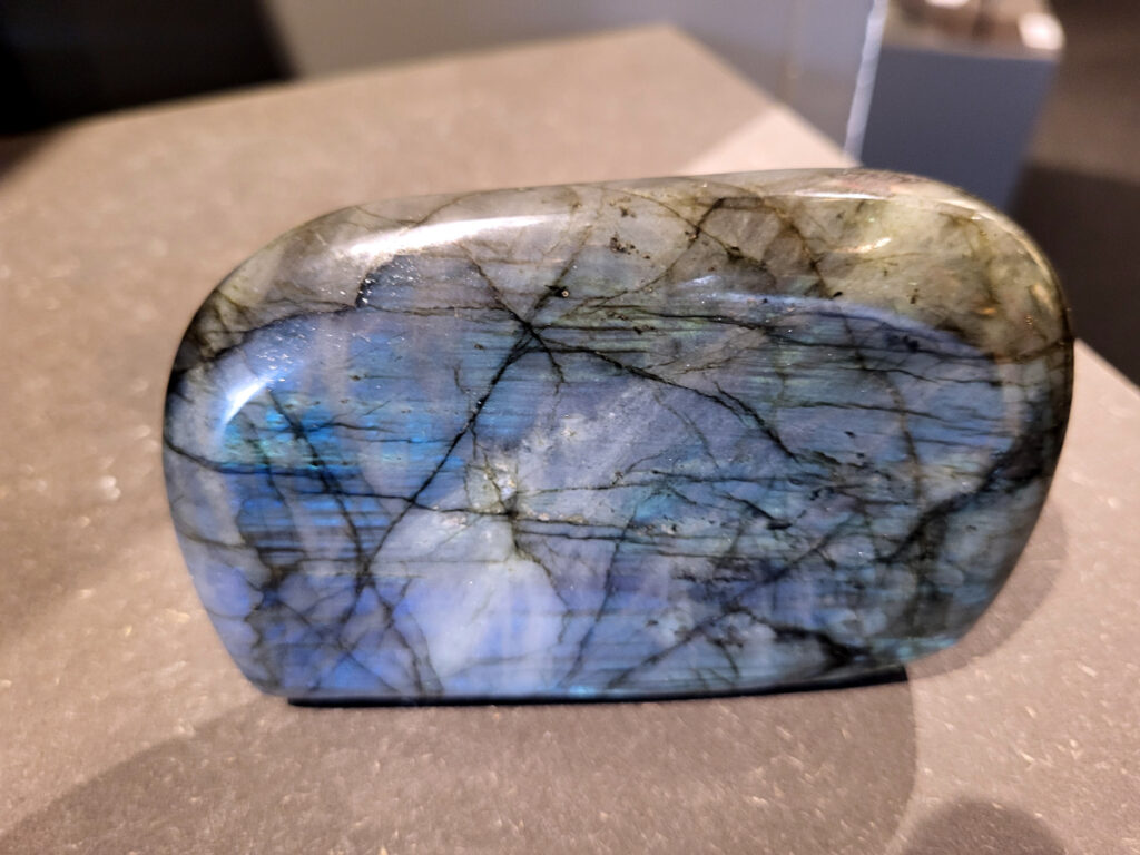 Labradoriet, 0,7kg, 12cm breed, 33,-euro, nr. 19
Beschrijving, Labradoriet.
Labradoriet is een edelsteen die bekend staat om zijn iriserende kleurenspel, ook wel labradoriseren genoemd, dat vaak doet denken aan het noorderlicht. Het is een populaire steen in de edelstenenwereld vanwege zowel zijn uiterlijk als zijn vermeende spirituele eigenschappen. 
Wat is labradoriet?
Labradoriet is een veldspaatmineraal dat wordt gekenmerkt door een opaalachtig glans of iriserend effect, veroorzaakt door de lichtbreking in de interne structuur van de steen.
De meest voorkomende kleur is grijs of groenachtig grijs, maar de steen kan ook blauwe, gele, oranje, paarse of zelfs rode flitsen laten zien.
De steen is genoemd naar het Canadese schiereiland Labrador, waar het voor het eerst werd ontdekt. 
Spirituele betekenis en eigenschappen:
Labradoriet wordt vaak beschouwd als een beschermende steen, vooral voor mensen die gevoelig zijn voor de energieën van hun omgeving. 
Het zou helpen bij het versterken van de aura en het verminderen van energielekkage, waardoor je je weerbaarder voelt. 
Labradoriet wordt geassocieerd met het versterken van intuïtie, het vergroten van het bewustzijn en het transformeren van negatieve energieën. 
Het wordt ook gebruikt om blokkades op te heffen en de innerlijke wijsheid te onthullen. 
Gebruik:
Labradoriet wordt vaak verwerkt in sieraden zoals hangers, armbanden en oorbellen. 
Het kan ook als ruwe steen, knuffelsteen of in andere vormen worden gebruikt, bijvoorbeeld in een huis of op een werkplek. 
Labradoriet kan worden gereinigd door het onder stromend water te houden of door het te reinigen met een andere steen zoals bergkristal of seleniet. 
Vindplaatsen:
Labradoriet wordt gevonden op verschillende locaties over de hele wereld, waaronder Canada, Finland, Madagaskar en Rusland. 
                                -Kunstgalerie Arnold-