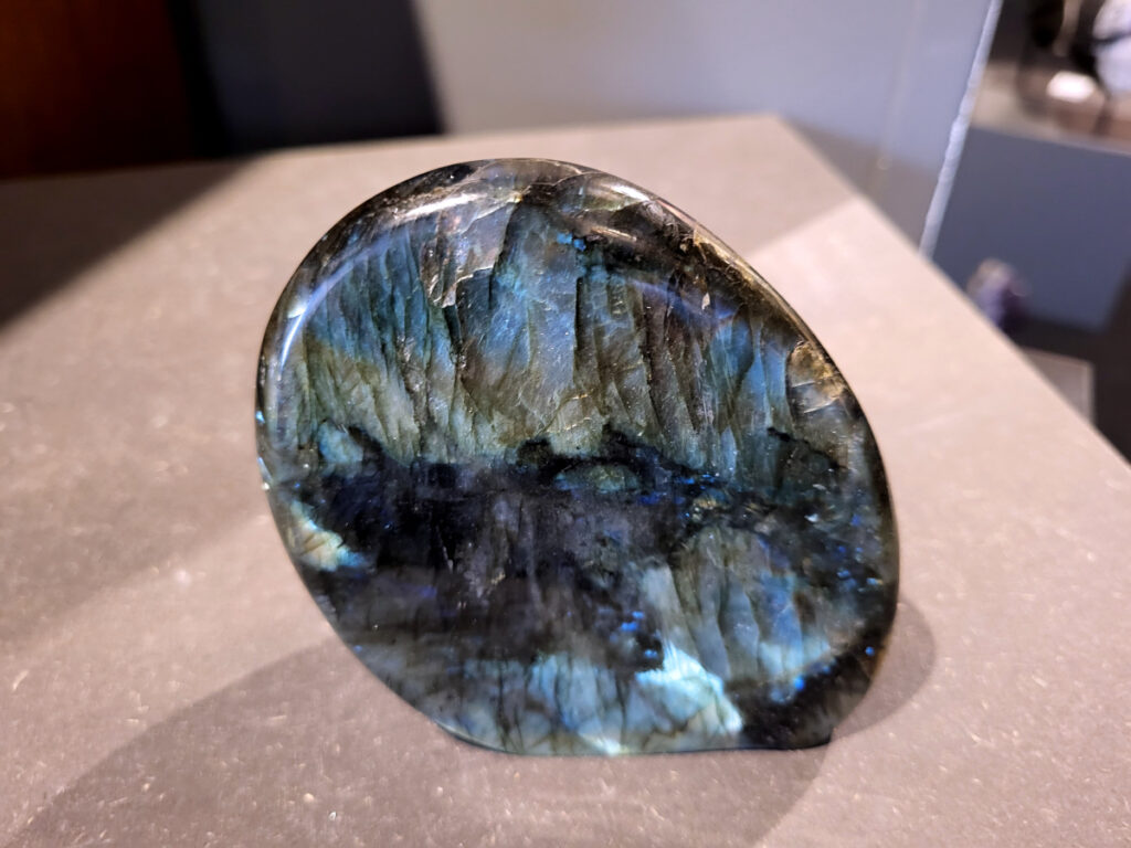 Labradoriet, 0,8kg, 11cm hoog, 38,- euro, nr. 18
Beschrijving, Labradoriet.
Labradoriet is een edelsteen die bekend staat om zijn iriserende kleurenspel, ook wel labradoriseren genoemd, dat vaak doet denken aan het noorderlicht. Het is een populaire steen in de edelstenenwereld vanwege zowel zijn uiterlijk als zijn vermeende spirituele eigenschappen. 
Wat is labradoriet?
Labradoriet is een veldspaatmineraal dat wordt gekenmerkt door een opaalachtig glans of iriserend effect, veroorzaakt door de lichtbreking in de interne structuur van de steen.
De meest voorkomende kleur is grijs of groenachtig grijs, maar de steen kan ook blauwe, gele, oranje, paarse of zelfs rode flitsen laten zien.
De steen is genoemd naar het Canadese schiereiland Labrador, waar het voor het eerst werd ontdekt. 
Spirituele betekenis en eigenschappen:
Labradoriet wordt vaak beschouwd als een beschermende steen, vooral voor mensen die gevoelig zijn voor de energieën van hun omgeving. 
Het zou helpen bij het versterken van de aura en het verminderen van energielekkage, waardoor je je weerbaarder voelt. 
Labradoriet wordt geassocieerd met het versterken van intuïtie, het vergroten van het bewustzijn en het transformeren van negatieve energieën. 
Het wordt ook gebruikt om blokkades op te heffen en de innerlijke wijsheid te onthullen. 
Gebruik:
Labradoriet wordt vaak verwerkt in sieraden zoals hangers, armbanden en oorbellen. 
Het kan ook als ruwe steen, knuffelsteen of in andere vormen worden gebruikt, bijvoorbeeld in een huis of op een werkplek. 
Labradoriet kan worden gereinigd door het onder stromend water te houden of door het te reinigen met een andere steen zoals bergkristal of seleniet. 
Vindplaatsen:
Labradoriet wordt gevonden op verschillende locaties over de hele wereld, waaronder Canada, Finland, Madagaskar en Rusland. 
                                -Kunstgalerie Arnold-