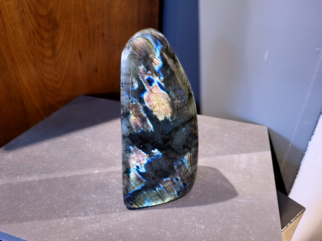 Labradoriet, 1,7kg, 18cm hoog, 59,- euro, nr. 16
Beschrijving, Labradoriet.
Labradoriet is een edelsteen die bekend staat om zijn iriserende kleurenspel, ook wel labradoriseren genoemd, dat vaak doet denken aan het noorderlicht. Het is een populaire steen in de edelstenenwereld vanwege zowel zijn uiterlijk als zijn vermeende spirituele eigenschappen. 
Wat is labradoriet?
Labradoriet is een veldspaatmineraal dat wordt gekenmerkt door een opaalachtig glans of iriserend effect, veroorzaakt door de lichtbreking in de interne structuur van de steen.
De meest voorkomende kleur is grijs of groenachtig grijs, maar de steen kan ook blauwe, gele, oranje, paarse of zelfs rode flitsen laten zien.
De steen is genoemd naar het Canadese schiereiland Labrador, waar het voor het eerst werd ontdekt. 
Spirituele betekenis en eigenschappen:
Labradoriet wordt vaak beschouwd als een beschermende steen, vooral voor mensen die gevoelig zijn voor de energieën van hun omgeving. 
Het zou helpen bij het versterken van de aura en het verminderen van energielekkage, waardoor je je weerbaarder voelt. 
Labradoriet wordt geassocieerd met het versterken van intuïtie, het vergroten van het bewustzijn en het transformeren van negatieve energieën. 
Het wordt ook gebruikt om blokkades op te heffen en de innerlijke wijsheid te onthullen. 
Gebruik:
Labradoriet wordt vaak verwerkt in sieraden zoals hangers, armbanden en oorbellen. 
Het kan ook als ruwe steen, knuffelsteen of in andere vormen worden gebruikt, bijvoorbeeld in een huis of op een werkplek. 
Labradoriet kan worden gereinigd door het onder stromend water te houden of door het te reinigen met een andere steen zoals bergkristal of seleniet. 
Vindplaatsen:
Labradoriet wordt gevonden op verschillende locaties over de hele wereld, waaronder Canada, Finland, Madagaskar en Rusland. 
                                -Kunstgalerie Arnold-