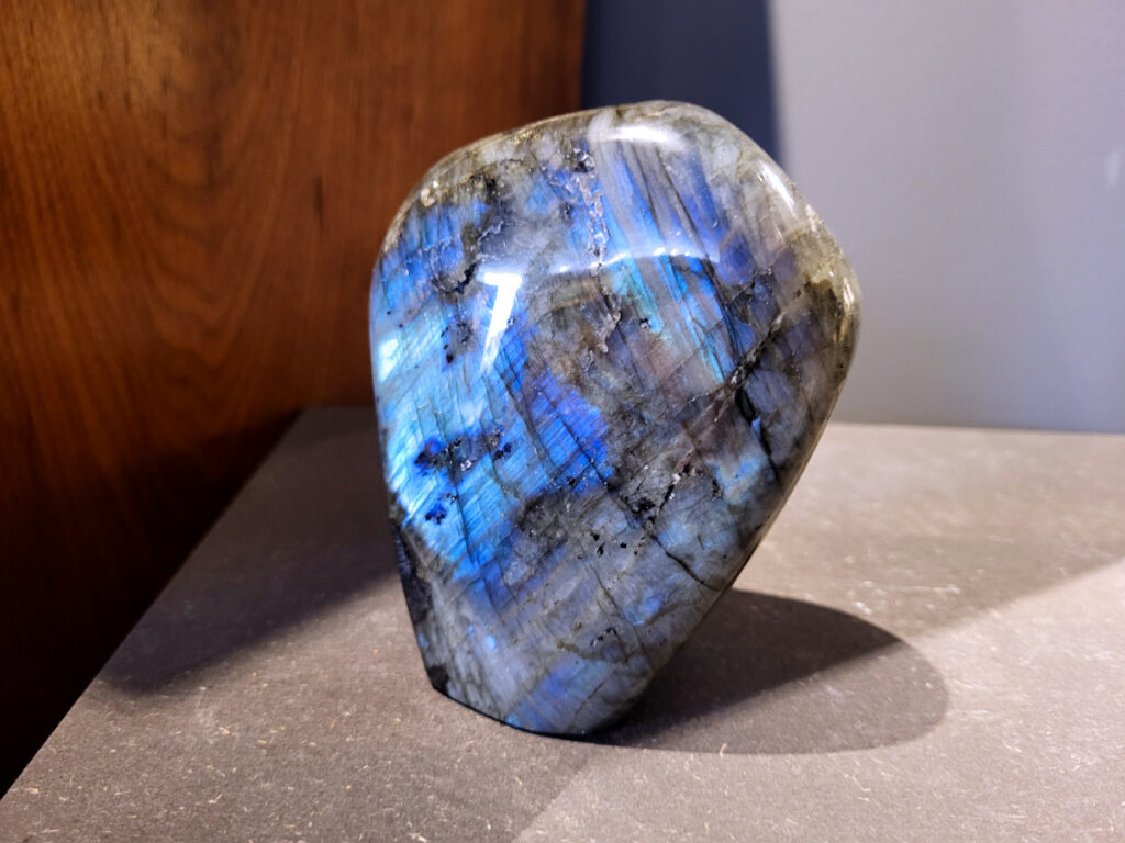 Labradoriet, 1kg, 12cm hoog, 31,- euro, nr. 10
Beschrijving, Labradoriet.
Labradoriet is een edelsteen die bekend staat om zijn iriserende kleurenspel, ook wel labradoriseren genoemd, dat vaak doet denken aan het noorderlicht. Het is een populaire steen in de edelstenenwereld vanwege zowel zijn uiterlijk als zijn vermeende spirituele eigenschappen. 
Wat is labradoriet?
Labradoriet is een veldspaatmineraal dat wordt gekenmerkt door een opaalachtig glans of iriserend effect, veroorzaakt door de lichtbreking in de interne structuur van de steen.
De meest voorkomende kleur is grijs of groenachtig grijs, maar de steen kan ook blauwe, gele, oranje, paarse of zelfs rode flitsen laten zien.
De steen is genoemd naar het Canadese schiereiland Labrador, waar het voor het eerst werd ontdekt. 
Spirituele betekenis en eigenschappen:
Labradoriet wordt vaak beschouwd als een beschermende steen, vooral voor mensen die gevoelig zijn voor de energieën van hun omgeving. 
Het zou helpen bij het versterken van de aura en het verminderen van energielekkage, waardoor je je weerbaarder voelt. 
Labradoriet wordt geassocieerd met het versterken van intuïtie, het vergroten van het bewustzijn en het transformeren van negatieve energieën. 
Het wordt ook gebruikt om blokkades op te heffen en de innerlijke wijsheid te onthullen. 
Gebruik:
Labradoriet wordt vaak verwerkt in sieraden zoals hangers, armbanden en oorbellen. 
Het kan ook als ruwe steen, knuffelsteen of in andere vormen worden gebruikt, bijvoorbeeld in een huis of op een werkplek. 
Labradoriet kan worden gereinigd door het onder stromend water te houden of door het te reinigen met een andere steen zoals bergkristal of seleniet. 
Vindplaatsen:
Labradoriet wordt gevonden op verschillende locaties over de hele wereld, waaronder Canada, Finland, Madagaskar en Rusland. 
                                -Kunstgalerie Arnold-