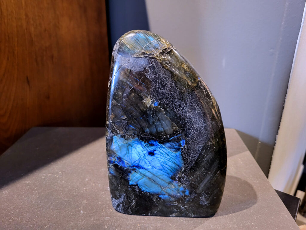 Labradoriet, 2,1kg, 18cm hoog, 65,- euro, nr. 6
Beschrijving, Labradoriet.
Labradoriet is een edelsteen die bekend staat om zijn iriserende kleurenspel, ook wel labradoriseren genoemd, dat vaak doet denken aan het noorderlicht. Het is een populaire steen in de edelstenenwereld vanwege zowel zijn uiterlijk als zijn vermeende spirituele eigenschappen. 
Wat is labradoriet?
Labradoriet is een veldspaatmineraal dat wordt gekenmerkt door een opaalachtig glans of iriserend effect, veroorzaakt door de lichtbreking in de interne structuur van de steen.
De meest voorkomende kleur is grijs of groenachtig grijs, maar de steen kan ook blauwe, gele, oranje, paarse of zelfs rode flitsen laten zien.
De steen is genoemd naar het Canadese schiereiland Labrador, waar het voor het eerst werd ontdekt. 
Spirituele betekenis en eigenschappen:
Labradoriet wordt vaak beschouwd als een beschermende steen, vooral voor mensen die gevoelig zijn voor de energieën van hun omgeving. 
Het zou helpen bij het versterken van de aura en het verminderen van energielekkage, waardoor je je weerbaarder voelt. 
Labradoriet wordt geassocieerd met het versterken van intuïtie, het vergroten van het bewustzijn en het transformeren van negatieve energieën. 
Het wordt ook gebruikt om blokkades op te heffen en de innerlijke wijsheid te onthullen. 
Gebruik:
Labradoriet wordt vaak verwerkt in sieraden zoals hangers, armbanden en oorbellen. 
Het kan ook als ruwe steen, knuffelsteen of in andere vormen worden gebruikt, bijvoorbeeld in een huis of op een werkplek. 
Labradoriet kan worden gereinigd door het onder stromend water te houden of door het te reinigen met een andere steen zoals bergkristal of seleniet. 
Vindplaatsen:
Labradoriet wordt gevonden op verschillende locaties over de hele wereld, waaronder Canada, Finland, Madagaskar en Rusland. 
                                -Kunstgalerie Arnold-