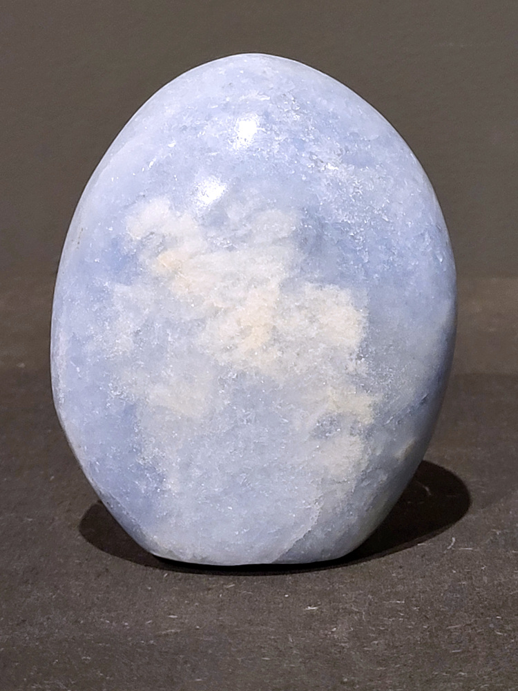 Blauwe calciet, 0,5kg, 10cm hoog, 16,- euro, nr. 15
Calciet is een veelvoorkomend mineraal dat voornamelijk bestaat uit calciumcarbonaat. Het komt in diverse kleuren en vormen voor en wordt in veel industrieën gebruikt, maar ook in de esoterie. 
Algemene kenmerken:
Samenstelling: Calciet bestaat voornamelijk uit calciumcarbonaat (CaCO3). 
Vorming: Het ontstaat door afzetting van calciumcarbonaat in water, maar ook door ophoping van schelpen en skeletten van zeedieren. 
Uiterlijk: Het heeft vaak een glasachtige glans, is doorzichtig tot doorschijnend en kan vele kleuren hebben, zoals geel, oranje, rood, bruin, blauw, groen, roze, wit en kleurloos. 
Hardheid: Calciet heeft een hardheid van 3 op de schaal van Mohs. 
Veelvoorkomend: Het is een van de meest voorkomende mineralen en is een hoofdbestanddeel van kalksteen, marmer en krijt. 
Esoterie:
In de edelsteentherapie wordt calciet gezien als een steen die energie versterkt, negatieve energieën verwijdert en spirituele groei bevordert. Verschillende kleuren calciet hebben specifieke eigenschappen, zoals gele calciet voor doorzettingsvermogen en moed, en mangano calciet voor emotionele heling. 
Specifieke calcietsoorten:
Gele Calciet: Staat bekend om het absorberen van negativiteit, het versterken van doorzettingsvermogen en het aantrekken van succes. 
Blauwe Calciet: Wordt geassocieerd met kalmering, communicatie en het loslaten van stress. 
Groene Calciet: Werkt op de hartchakra, bevordert liefde, compassie en emotionele heling. 
Mangano Calciet: Wordt gebruikt voor emotionele heling, het loslaten van oud verdriet en het versterken van zelfvertrouwen. 
Reiniging:
Calciet kan op verschillende manieren gereinigd worden, maar het is belangrijk om te weten dat sommige soorten, zoals gele calciet, niet goed tegen water kunnen. 
Andere reinigingsmethoden zijn bijvoorbeeld reinigen met edelstenenspray, op een Amethist of bergkristal leggen, of reinigen met selenite. 
Het is een steen die kan worden gebruikt voor energieversterking, emotionele heling en het bevorderen van spirituele groei, afhankelijk van de specifieke kleur en eigenschappen. 
                                                    -Kunstgalerie Arnold-