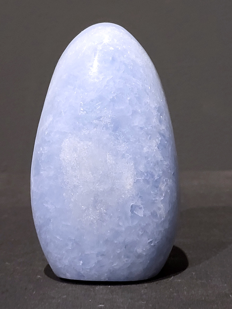 Blauwe calciet, 0,5kg, 11cm hoog, 16,- euro, nr. 2
Calciet is een veelvoorkomend mineraal dat voornamelijk bestaat uit calciumcarbonaat. Het komt in diverse kleuren en vormen voor en wordt in veel industrieën gebruikt, maar ook in de esoterie. 
Algemene kenmerken:
Samenstelling: Calciet bestaat voornamelijk uit calciumcarbonaat (CaCO3). 
Vorming: Het ontstaat door afzetting van calciumcarbonaat in water, maar ook door ophoping van schelpen en skeletten van zeedieren. 
Uiterlijk: Het heeft vaak een glasachtige glans, is doorzichtig tot doorschijnend en kan vele kleuren hebben, zoals geel, oranje, rood, bruin, blauw, groen, roze, wit en kleurloos. 
Hardheid: Calciet heeft een hardheid van 3 op de schaal van Mohs. 
Veelvoorkomend: Het is een van de meest voorkomende mineralen en is een hoofdbestanddeel van kalksteen, marmer en krijt. 
Esoterie:
In de edelsteentherapie wordt calciet gezien als een steen die energie versterkt, negatieve energieën verwijdert en spirituele groei bevordert. Verschillende kleuren calciet hebben specifieke eigenschappen, zoals gele calciet voor doorzettingsvermogen en moed, en mangano calciet voor emotionele heling. 
Specifieke calcietsoorten:
Gele Calciet: Staat bekend om het absorberen van negativiteit, het versterken van doorzettingsvermogen en het aantrekken van succes. 
Blauwe Calciet: Wordt geassocieerd met kalmering, communicatie en het loslaten van stress. 
Groene Calciet: Werkt op de hartchakra, bevordert liefde, compassie en emotionele heling. 
Mangano Calciet: Wordt gebruikt voor emotionele heling, het loslaten van oud verdriet en het versterken van zelfvertrouwen. 
Reiniging:
Calciet kan op verschillende manieren gereinigd worden, maar het is belangrijk om te weten dat sommige soorten, zoals gele calciet, niet goed tegen water kunnen. 
Andere reinigingsmethoden zijn bijvoorbeeld reinigen met edelstenenspray, op een Amethist of bergkristal leggen, of reinigen met selenite. 
Het is een steen die kan worden gebruikt voor energieversterking, emotionele heling en het bevorderen van spirituele groei, afhankelijk van de specifieke kleur en eigenschappen. 
                                                    -Kunstgalerie Arnold-