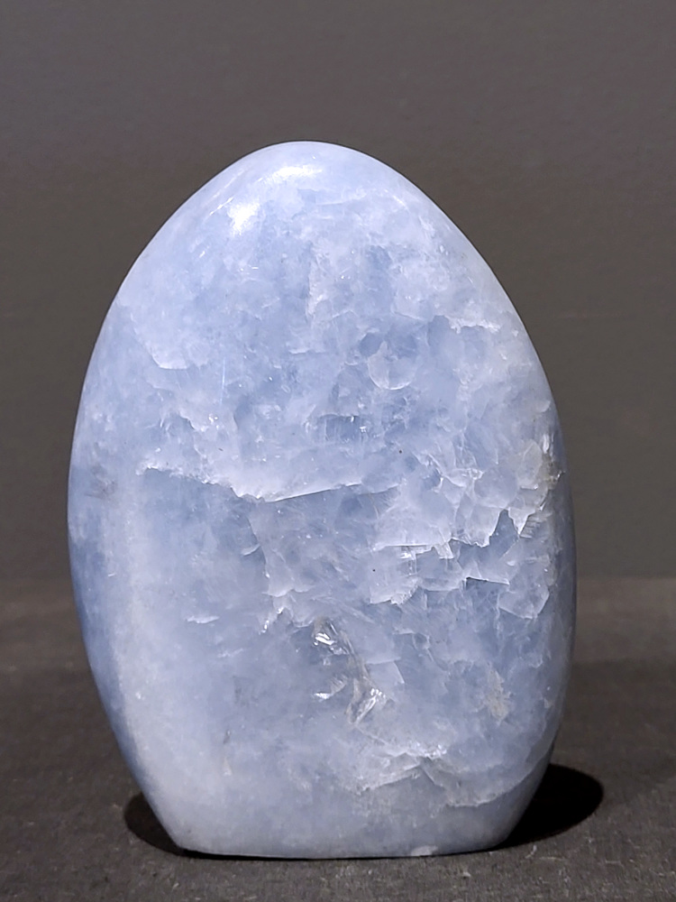 Blauwe calciet, 0,6kg, 12cm hoog, 17,- euro, nr. 3
Calciet is een veelvoorkomend mineraal dat voornamelijk bestaat uit calciumcarbonaat. Het komt in diverse kleuren en vormen voor en wordt in veel industrieën gebruikt, maar ook in de esoterie. 
Algemene kenmerken:
Samenstelling: Calciet bestaat voornamelijk uit calciumcarbonaat (CaCO3). 
Vorming: Het ontstaat door afzetting van calciumcarbonaat in water, maar ook door ophoping van schelpen en skeletten van zeedieren. 
Uiterlijk: Het heeft vaak een glasachtige glans, is doorzichtig tot doorschijnend en kan vele kleuren hebben, zoals geel, oranje, rood, bruin, blauw, groen, roze, wit en kleurloos. 
Hardheid: Calciet heeft een hardheid van 3 op de schaal van Mohs. 
Veelvoorkomend: Het is een van de meest voorkomende mineralen en is een hoofdbestanddeel van kalksteen, marmer en krijt. 
Esoterie:
In de edelsteentherapie wordt calciet gezien als een steen die energie versterkt, negatieve energieën verwijdert en spirituele groei bevordert. Verschillende kleuren calciet hebben specifieke eigenschappen, zoals gele calciet voor doorzettingsvermogen en moed, en mangano calciet voor emotionele heling. 
Specifieke calcietsoorten:
Gele Calciet: Staat bekend om het absorberen van negativiteit, het versterken van doorzettingsvermogen en het aantrekken van succes. 
Blauwe Calciet: Wordt geassocieerd met kalmering, communicatie en het loslaten van stress. 
Groene Calciet: Werkt op de hartchakra, bevordert liefde, compassie en emotionele heling. 
Mangano Calciet: Wordt gebruikt voor emotionele heling, het loslaten van oud verdriet en het versterken van zelfvertrouwen. 
Reiniging:
Calciet kan op verschillende manieren gereinigd worden, maar het is belangrijk om te weten dat sommige soorten, zoals gele calciet, niet goed tegen water kunnen. 
Andere reinigingsmethoden zijn bijvoorbeeld reinigen met edelstenenspray, op een Amethist of bergkristal leggen, of reinigen met selenite. 
Het is een steen die kan worden gebruikt voor energieversterking, emotionele heling en het bevorderen van spirituele groei, afhankelijk van de specifieke kleur en eigenschappen. 
                                                    -Kunstgalerie Arnold-