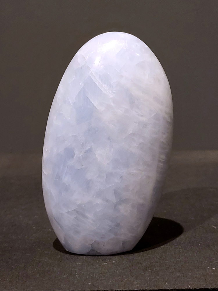 Blauwe calciet, 0,6kg, 12cm hoog, 18,- euro, nr. 4
Calciet is een veelvoorkomend mineraal dat voornamelijk bestaat uit calciumcarbonaat. Het komt in diverse kleuren en vormen voor en wordt in veel industrieën gebruikt, maar ook in de esoterie. 
Algemene kenmerken:
Samenstelling: Calciet bestaat voornamelijk uit calciumcarbonaat (CaCO3). 
Vorming: Het ontstaat door afzetting van calciumcarbonaat in water, maar ook door ophoping van schelpen en skeletten van zeedieren. 
Uiterlijk: Het heeft vaak een glasachtige glans, is doorzichtig tot doorschijnend en kan vele kleuren hebben, zoals geel, oranje, rood, bruin, blauw, groen, roze, wit en kleurloos. 
Hardheid: Calciet heeft een hardheid van 3 op de schaal van Mohs. 
Veelvoorkomend: Het is een van de meest voorkomende mineralen en is een hoofdbestanddeel van kalksteen, marmer en krijt. 
Esoterie:
In de edelsteentherapie wordt calciet gezien als een steen die energie versterkt, negatieve energieën verwijdert en spirituele groei bevordert. Verschillende kleuren calciet hebben specifieke eigenschappen, zoals gele calciet voor doorzettingsvermogen en moed, en mangano calciet voor emotionele heling. 
Specifieke calcietsoorten:
Gele Calciet: Staat bekend om het absorberen van negativiteit, het versterken van doorzettingsvermogen en het aantrekken van succes. 
Blauwe Calciet: Wordt geassocieerd met kalmering, communicatie en het loslaten van stress. 
Groene Calciet: Werkt op de hartchakra, bevordert liefde, compassie en emotionele heling. 
Mangano Calciet: Wordt gebruikt voor emotionele heling, het loslaten van oud verdriet en het versterken van zelfvertrouwen. 
Reiniging:
Calciet kan op verschillende manieren gereinigd worden, maar het is belangrijk om te weten dat sommige soorten, zoals gele calciet, niet goed tegen water kunnen. 
Andere reinigingsmethoden zijn bijvoorbeeld reinigen met edelstenenspray, op een Amethist of bergkristal leggen, of reinigen met selenite. 
Het is een steen die kan worden gebruikt voor energieversterking, emotionele heling en het bevorderen van spirituele groei, afhankelijk van de specifieke kleur en eigenschappen. 
                                                    -Kunstgalerie Arnold-