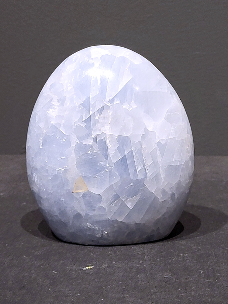 Blauwe calciet, 0,7kg, 10cm hoog, 21,- euro, nr. 17
Calciet is een veelvoorkomend mineraal dat voornamelijk bestaat uit calciumcarbonaat. Het komt in diverse kleuren en vormen voor en wordt in veel industrieën gebruikt, maar ook in de esoterie. 
Algemene kenmerken:
Samenstelling: Calciet bestaat voornamelijk uit calciumcarbonaat (CaCO3). 
Vorming: Het ontstaat door afzetting van calciumcarbonaat in water, maar ook door ophoping van schelpen en skeletten van zeedieren. 
Uiterlijk: Het heeft vaak een glasachtige glans, is doorzichtig tot doorschijnend en kan vele kleuren hebben, zoals geel, oranje, rood, bruin, blauw, groen, roze, wit en kleurloos. 
Hardheid: Calciet heeft een hardheid van 3 op de schaal van Mohs. 
Veelvoorkomend: Het is een van de meest voorkomende mineralen en is een hoofdbestanddeel van kalksteen, marmer en krijt. 
Esoterie:
In de edelsteentherapie wordt calciet gezien als een steen die energie versterkt, negatieve energieën verwijdert en spirituele groei bevordert. Verschillende kleuren calciet hebben specifieke eigenschappen, zoals gele calciet voor doorzettingsvermogen en moed, en mangano calciet voor emotionele heling. 
Specifieke calcietsoorten:
Gele Calciet: Staat bekend om het absorberen van negativiteit, het versterken van doorzettingsvermogen en het aantrekken van succes. 
Blauwe Calciet: Wordt geassocieerd met kalmering, communicatie en het loslaten van stress. 
Groene Calciet: Werkt op de hartchakra, bevordert liefde, compassie en emotionele heling. 
Mangano Calciet: Wordt gebruikt voor emotionele heling, het loslaten van oud verdriet en het versterken van zelfvertrouwen. 
Reiniging:
Calciet kan op verschillende manieren gereinigd worden, maar het is belangrijk om te weten dat sommige soorten, zoals gele calciet, niet goed tegen water kunnen. 
Andere reinigingsmethoden zijn bijvoorbeeld reinigen met edelstenenspray, op een Amethist of bergkristal leggen, of reinigen met selenite. 
Het is een steen die kan worden gebruikt voor energieversterking, emotionele heling en het bevorderen van spirituele groei, afhankelijk van de specifieke kleur en eigenschappen. 
                                                    -Kunstgalerie Arnold-