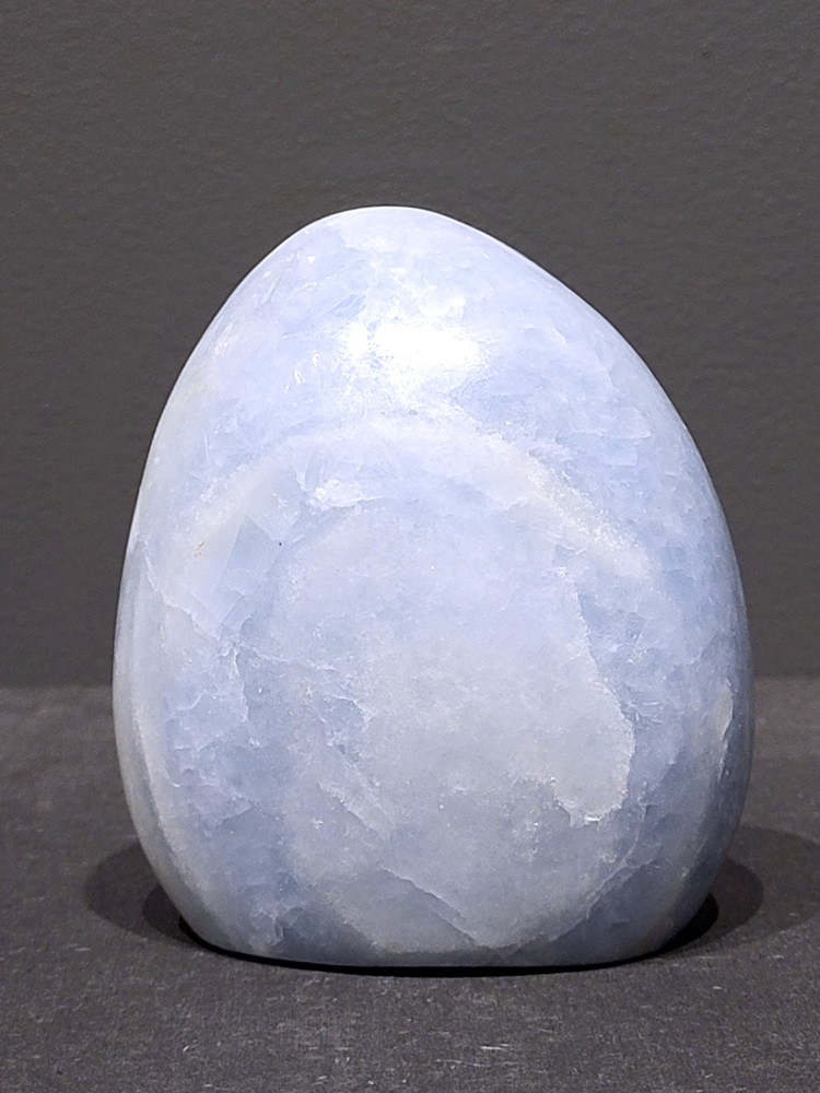 Blauwe calciet, 0,7kg, 10cm hoog, 22,- euro, nr. 5
Calciet is een veelvoorkomend mineraal dat voornamelijk bestaat uit calciumcarbonaat. Het komt in diverse kleuren en vormen voor en wordt in veel industrieën gebruikt, maar ook in de esoterie. 
Algemene kenmerken:
Samenstelling: Calciet bestaat voornamelijk uit calciumcarbonaat (CaCO3). 
Vorming: Het ontstaat door afzetting van calciumcarbonaat in water, maar ook door ophoping van schelpen en skeletten van zeedieren. 
Uiterlijk: Het heeft vaak een glasachtige glans, is doorzichtig tot doorschijnend en kan vele kleuren hebben, zoals geel, oranje, rood, bruin, blauw, groen, roze, wit en kleurloos. 
Hardheid: Calciet heeft een hardheid van 3 op de schaal van Mohs. 
Veelvoorkomend: Het is een van de meest voorkomende mineralen en is een hoofdbestanddeel van kalksteen, marmer en krijt. 
Esoterie:
In de edelsteentherapie wordt calciet gezien als een steen die energie versterkt, negatieve energieën verwijdert en spirituele groei bevordert. Verschillende kleuren calciet hebben specifieke eigenschappen, zoals gele calciet voor doorzettingsvermogen en moed, en mangano calciet voor emotionele heling. 
Specifieke calcietsoorten:
Gele Calciet: Staat bekend om het absorberen van negativiteit, het versterken van doorzettingsvermogen en het aantrekken van succes. 
Blauwe Calciet: Wordt geassocieerd met kalmering, communicatie en het loslaten van stress. 
Groene Calciet: Werkt op de hartchakra, bevordert liefde, compassie en emotionele heling. 
Mangano Calciet: Wordt gebruikt voor emotionele heling, het loslaten van oud verdriet en het versterken van zelfvertrouwen. 
Reiniging:
Calciet kan op verschillende manieren gereinigd worden, maar het is belangrijk om te weten dat sommige soorten, zoals gele calciet, niet goed tegen water kunnen. 
Andere reinigingsmethoden zijn bijvoorbeeld reinigen met edelstenenspray, op een Amethist of bergkristal leggen, of reinigen met selenite. 
Het is een steen die kan worden gebruikt voor energieversterking, emotionele heling en het bevorderen van spirituele groei, afhankelijk van de specifieke kleur en eigenschappen. 
                                                    -Kunstgalerie Arnold-