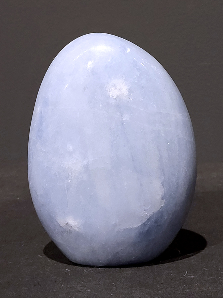 Blauwe calciet, 0,7kg, 11cm hoog, 21,- euro, nr. 6
Calciet is een veelvoorkomend mineraal dat voornamelijk bestaat uit calciumcarbonaat. Het komt in diverse kleuren en vormen voor en wordt in veel industrieën gebruikt, maar ook in de esoterie. 
Algemene kenmerken:
Samenstelling: Calciet bestaat voornamelijk uit calciumcarbonaat (CaCO3). 
Vorming: Het ontstaat door afzetting van calciumcarbonaat in water, maar ook door ophoping van schelpen en skeletten van zeedieren. 
Uiterlijk: Het heeft vaak een glasachtige glans, is doorzichtig tot doorschijnend en kan vele kleuren hebben, zoals geel, oranje, rood, bruin, blauw, groen, roze, wit en kleurloos. 
Hardheid: Calciet heeft een hardheid van 3 op de schaal van Mohs. 
Veelvoorkomend: Het is een van de meest voorkomende mineralen en is een hoofdbestanddeel van kalksteen, marmer en krijt. 
Esoterie:
In de edelsteentherapie wordt calciet gezien als een steen die energie versterkt, negatieve energieën verwijdert en spirituele groei bevordert. Verschillende kleuren calciet hebben specifieke eigenschappen, zoals gele calciet voor doorzettingsvermogen en moed, en mangano calciet voor emotionele heling. 
Specifieke calcietsoorten:
Gele Calciet: Staat bekend om het absorberen van negativiteit, het versterken van doorzettingsvermogen en het aantrekken van succes. 
Blauwe Calciet: Wordt geassocieerd met kalmering, communicatie en het loslaten van stress. 
Groene Calciet: Werkt op de hartchakra, bevordert liefde, compassie en emotionele heling. 
Mangano Calciet: Wordt gebruikt voor emotionele heling, het loslaten van oud verdriet en het versterken van zelfvertrouwen. 
Reiniging:
Calciet kan op verschillende manieren gereinigd worden, maar het is belangrijk om te weten dat sommige soorten, zoals gele calciet, niet goed tegen water kunnen. 
Andere reinigingsmethoden zijn bijvoorbeeld reinigen met edelstenenspray, op een Amethist of bergkristal leggen, of reinigen met selenite. 
Het is een steen die kan worden gebruikt voor energieversterking, emotionele heling en het bevorderen van spirituele groei, afhankelijk van de specifieke kleur en eigenschappen. 
                                                    -Kunstgalerie Arnold-