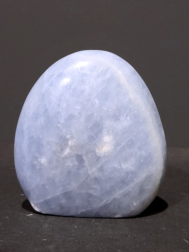 Blauwe calciet, 0,7kg, 11cm hoog, 22,- euro, nr. 7
Calciet is een veelvoorkomend mineraal dat voornamelijk bestaat uit calciumcarbonaat. Het komt in diverse kleuren en vormen voor en wordt in veel industrieën gebruikt, maar ook in de esoterie. 
Algemene kenmerken:
Samenstelling: Calciet bestaat voornamelijk uit calciumcarbonaat (CaCO3). 
Vorming: Het ontstaat door afzetting van calciumcarbonaat in water, maar ook door ophoping van schelpen en skeletten van zeedieren. 
Uiterlijk: Het heeft vaak een glasachtige glans, is doorzichtig tot doorschijnend en kan vele kleuren hebben, zoals geel, oranje, rood, bruin, blauw, groen, roze, wit en kleurloos. 
Hardheid: Calciet heeft een hardheid van 3 op de schaal van Mohs. 
Veelvoorkomend: Het is een van de meest voorkomende mineralen en is een hoofdbestanddeel van kalksteen, marmer en krijt. 
Esoterie:
In de edelsteentherapie wordt calciet gezien als een steen die energie versterkt, negatieve energieën verwijdert en spirituele groei bevordert. Verschillende kleuren calciet hebben specifieke eigenschappen, zoals gele calciet voor doorzettingsvermogen en moed, en mangano calciet voor emotionele heling. 
Specifieke calcietsoorten:
Gele Calciet: Staat bekend om het absorberen van negativiteit, het versterken van doorzettingsvermogen en het aantrekken van succes. 
Blauwe Calciet: Wordt geassocieerd met kalmering, communicatie en het loslaten van stress. 
Groene Calciet: Werkt op de hartchakra, bevordert liefde, compassie en emotionele heling. 
Mangano Calciet: Wordt gebruikt voor emotionele heling, het loslaten van oud verdriet en het versterken van zelfvertrouwen. 
Reiniging:
Calciet kan op verschillende manieren gereinigd worden, maar het is belangrijk om te weten dat sommige soorten, zoals gele calciet, niet goed tegen water kunnen. 
Andere reinigingsmethoden zijn bijvoorbeeld reinigen met edelstenenspray, op een Amethist of bergkristal leggen, of reinigen met selenite. 
Het is een steen die kan worden gebruikt voor energieversterking, emotionele heling en het bevorderen van spirituele groei, afhankelijk van de specifieke kleur en eigenschappen. 
                                                    -Kunstgalerie Arnold-