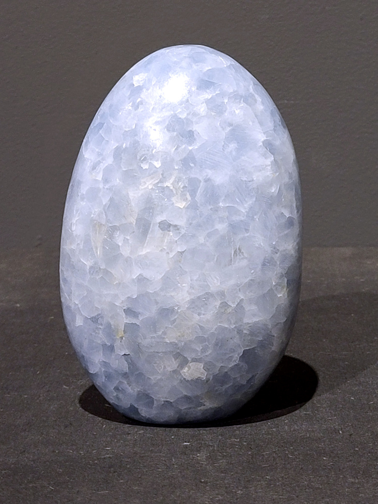 Blauwe calciet, 0,7kg, 12cm hoog, 21,- euro, nr. 8
Calciet is een veelvoorkomend mineraal dat voornamelijk bestaat uit calciumcarbonaat. Het komt in diverse kleuren en vormen voor en wordt in veel industrieën gebruikt, maar ook in de esoterie. 
Algemene kenmerken:
Samenstelling: Calciet bestaat voornamelijk uit calciumcarbonaat (CaCO3). 
Vorming: Het ontstaat door afzetting van calciumcarbonaat in water, maar ook door ophoping van schelpen en skeletten van zeedieren. 
Uiterlijk: Het heeft vaak een glasachtige glans, is doorzichtig tot doorschijnend en kan vele kleuren hebben, zoals geel, oranje, rood, bruin, blauw, groen, roze, wit en kleurloos. 
Hardheid: Calciet heeft een hardheid van 3 op de schaal van Mohs. 
Veelvoorkomend: Het is een van de meest voorkomende mineralen en is een hoofdbestanddeel van kalksteen, marmer en krijt. 
Esoterie:
In de edelsteentherapie wordt calciet gezien als een steen die energie versterkt, negatieve energieën verwijdert en spirituele groei bevordert. Verschillende kleuren calciet hebben specifieke eigenschappen, zoals gele calciet voor doorzettingsvermogen en moed, en mangano calciet voor emotionele heling. 
Specifieke calcietsoorten:
Gele Calciet: Staat bekend om het absorberen van negativiteit, het versterken van doorzettingsvermogen en het aantrekken van succes. 
Blauwe Calciet: Wordt geassocieerd met kalmering, communicatie en het loslaten van stress. 
Groene Calciet: Werkt op de hartchakra, bevordert liefde, compassie en emotionele heling. 
Mangano Calciet: Wordt gebruikt voor emotionele heling, het loslaten van oud verdriet en het versterken van zelfvertrouwen. 
Reiniging:
Calciet kan op verschillende manieren gereinigd worden, maar het is belangrijk om te weten dat sommige soorten, zoals gele calciet, niet goed tegen water kunnen. 
Andere reinigingsmethoden zijn bijvoorbeeld reinigen met edelstenenspray, op een Amethist of bergkristal leggen, of reinigen met selenite. 
Het is een steen die kan worden gebruikt voor energieversterking, emotionele heling en het bevorderen van spirituele groei, afhankelijk van de specifieke kleur en eigenschappen. 
                                                    -Kunstgalerie Arnold-