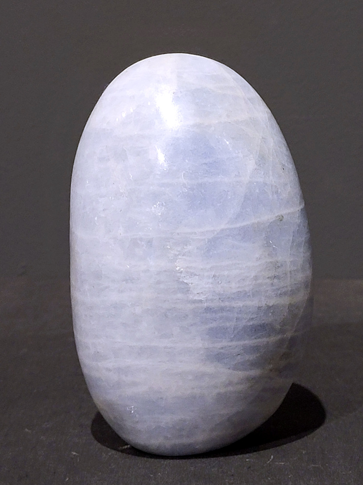 Blauwe calciet, 0,7kg, 12cm hoog, 21,- euro, nr. 18
Calciet is een veelvoorkomend mineraal dat voornamelijk bestaat uit calciumcarbonaat. Het komt in diverse kleuren en vormen voor en wordt in veel industrieën gebruikt, maar ook in de esoterie. 
Algemene kenmerken:
Samenstelling: Calciet bestaat voornamelijk uit calciumcarbonaat (CaCO3). 
Vorming: Het ontstaat door afzetting van calciumcarbonaat in water, maar ook door ophoping van schelpen en skeletten van zeedieren. 
Uiterlijk: Het heeft vaak een glasachtige glans, is doorzichtig tot doorschijnend en kan vele kleuren hebben, zoals geel, oranje, rood, bruin, blauw, groen, roze, wit en kleurloos. 
Hardheid: Calciet heeft een hardheid van 3 op de schaal van Mohs. 
Veelvoorkomend: Het is een van de meest voorkomende mineralen en is een hoofdbestanddeel van kalksteen, marmer en krijt. 
Esoterie:
In de edelsteentherapie wordt calciet gezien als een steen die energie versterkt, negatieve energieën verwijdert en spirituele groei bevordert. Verschillende kleuren calciet hebben specifieke eigenschappen, zoals gele calciet voor doorzettingsvermogen en moed, en mangano calciet voor emotionele heling. 
Specifieke calcietsoorten:
Gele Calciet: Staat bekend om het absorberen van negativiteit, het versterken van doorzettingsvermogen en het aantrekken van succes. 
Blauwe Calciet: Wordt geassocieerd met kalmering, communicatie en het loslaten van stress. 
Groene Calciet: Werkt op de hartchakra, bevordert liefde, compassie en emotionele heling. 
Mangano Calciet: Wordt gebruikt voor emotionele heling, het loslaten van oud verdriet en het versterken van zelfvertrouwen. 
Reiniging:
Calciet kan op verschillende manieren gereinigd worden, maar het is belangrijk om te weten dat sommige soorten, zoals gele calciet, niet goed tegen water kunnen. 
Andere reinigingsmethoden zijn bijvoorbeeld reinigen met edelstenenspray, op een Amethist of bergkristal leggen, of reinigen met selenite. 
Het is een steen die kan worden gebruikt voor energieversterking, emotionele heling en het bevorderen van spirituele groei, afhankelijk van de specifieke kleur en eigenschappen. 
                                                    -Kunstgalerie Arnold-