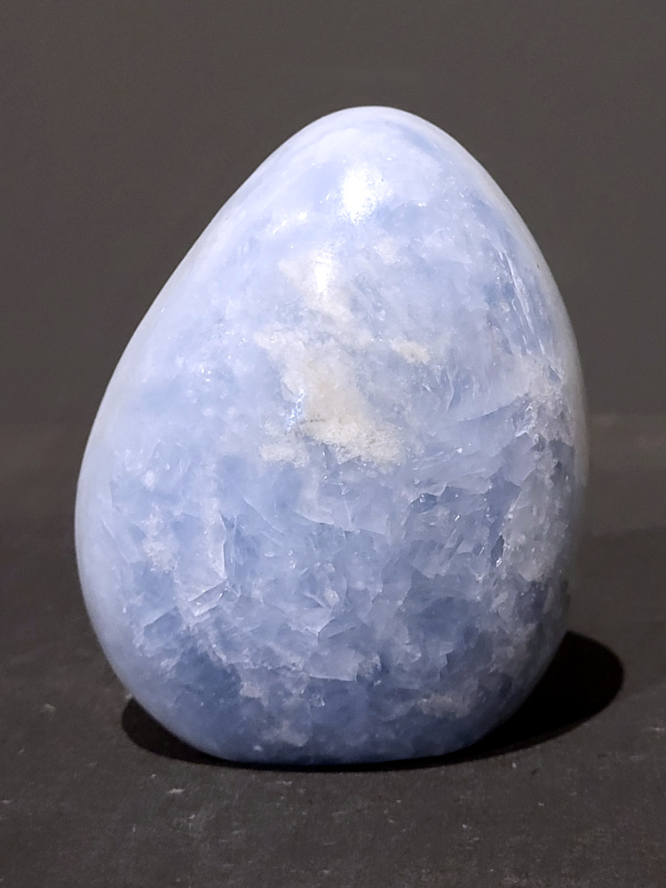 Blauwe calciet, 0,8kg, 10cm hoog, 23,- euro, nr. 19
Calciet is een veelvoorkomend mineraal dat voornamelijk bestaat uit calciumcarbonaat. Het komt in diverse kleuren en vormen voor en wordt in veel industrieën gebruikt, maar ook in de esoterie. 
Algemene kenmerken:
Samenstelling: Calciet bestaat voornamelijk uit calciumcarbonaat (CaCO3). 
Vorming: Het ontstaat door afzetting van calciumcarbonaat in water, maar ook door ophoping van schelpen en skeletten van zeedieren. 
Uiterlijk: Het heeft vaak een glasachtige glans, is doorzichtig tot doorschijnend en kan vele kleuren hebben, zoals geel, oranje, rood, bruin, blauw, groen, roze, wit en kleurloos. 
Hardheid: Calciet heeft een hardheid van 3 op de schaal van Mohs. 
Veelvoorkomend: Het is een van de meest voorkomende mineralen en is een hoofdbestanddeel van kalksteen, marmer en krijt. 
Esoterie:
In de edelsteentherapie wordt calciet gezien als een steen die energie versterkt, negatieve energieën verwijdert en spirituele groei bevordert. Verschillende kleuren calciet hebben specifieke eigenschappen, zoals gele calciet voor doorzettingsvermogen en moed, en mangano calciet voor emotionele heling. 
Specifieke calcietsoorten:
Gele Calciet: Staat bekend om het absorberen van negativiteit, het versterken van doorzettingsvermogen en het aantrekken van succes. 
Blauwe Calciet: Wordt geassocieerd met kalmering, communicatie en het loslaten van stress. 
Groene Calciet: Werkt op de hartchakra, bevordert liefde, compassie en emotionele heling. 
Mangano Calciet: Wordt gebruikt voor emotionele heling, het loslaten van oud verdriet en het versterken van zelfvertrouwen. 
Reiniging:
Calciet kan op verschillende manieren gereinigd worden, maar het is belangrijk om te weten dat sommige soorten, zoals gele calciet, niet goed tegen water kunnen. 
Andere reinigingsmethoden zijn bijvoorbeeld reinigen met edelstenenspray, op een Amethist of bergkristal leggen, of reinigen met selenite. 
Het is een steen die kan worden gebruikt voor energieversterking, emotionele heling en het bevorderen van spirituele groei, afhankelijk van de specifieke kleur en eigenschappen. 
                                                    -Kunstgalerie Arnold-