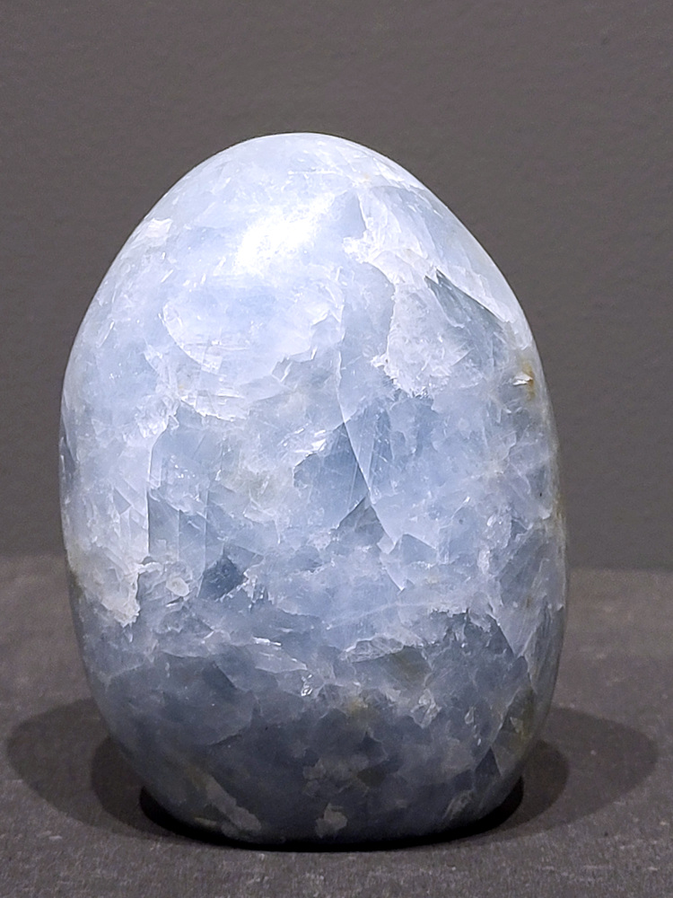 Blauwe calciet, 0,8kg, 11cm hoog, 24,-euro, nr. 10
Calciet is een veelvoorkomend mineraal dat voornamelijk bestaat uit calciumcarbonaat. Het komt in diverse kleuren en vormen voor en wordt in veel industrieën gebruikt, maar ook in de esoterie. 
Algemene kenmerken:
Samenstelling: Calciet bestaat voornamelijk uit calciumcarbonaat (CaCO3). 
Vorming: Het ontstaat door afzetting van calciumcarbonaat in water, maar ook door ophoping van schelpen en skeletten van zeedieren. 
Uiterlijk: Het heeft vaak een glasachtige glans, is doorzichtig tot doorschijnend en kan vele kleuren hebben, zoals geel, oranje, rood, bruin, blauw, groen, roze, wit en kleurloos. 
Hardheid: Calciet heeft een hardheid van 3 op de schaal van Mohs. 
Veelvoorkomend: Het is een van de meest voorkomende mineralen en is een hoofdbestanddeel van kalksteen, marmer en krijt. 
Esoterie:
In de edelsteentherapie wordt calciet gezien als een steen die energie versterkt, negatieve energieën verwijdert en spirituele groei bevordert. Verschillende kleuren calciet hebben specifieke eigenschappen, zoals gele calciet voor doorzettingsvermogen en moed, en mangano calciet voor emotionele heling. 
Specifieke calcietsoorten:
Gele Calciet: Staat bekend om het absorberen van negativiteit, het versterken van doorzettingsvermogen en het aantrekken van succes. 
Blauwe Calciet: Wordt geassocieerd met kalmering, communicatie en het loslaten van stress. 
Groene Calciet: Werkt op de hartchakra, bevordert liefde, compassie en emotionele heling. 
Mangano Calciet: Wordt gebruikt voor emotionele heling, het loslaten van oud verdriet en het versterken van zelfvertrouwen. 
Reiniging:
Calciet kan op verschillende manieren gereinigd worden, maar het is belangrijk om te weten dat sommige soorten, zoals gele calciet, niet goed tegen water kunnen. 
Andere reinigingsmethoden zijn bijvoorbeeld reinigen met edelstenenspray, op een Amethist of bergkristal leggen, of reinigen met selenite. 
Het is een steen die kan worden gebruikt voor energieversterking, emotionele heling en het bevorderen van spirituele groei, afhankelijk van de specifieke kleur en eigenschappen.