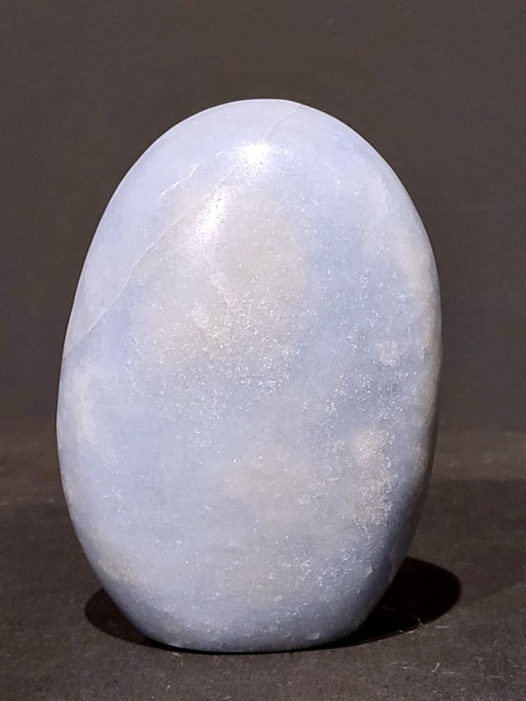 Blauwe calciet, 0,8kg, 12cm hoog, 23,- euro, nr. 21
Calciet is een veelvoorkomend mineraal dat voornamelijk bestaat uit calciumcarbonaat. Het komt in diverse kleuren en vormen voor en wordt in veel industrieën gebruikt, maar ook in de esoterie. 
Algemene kenmerken:
Samenstelling: Calciet bestaat voornamelijk uit calciumcarbonaat (CaCO3). 
Vorming: Het ontstaat door afzetting van calciumcarbonaat in water, maar ook door ophoping van schelpen en skeletten van zeedieren. 
Uiterlijk: Het heeft vaak een glasachtige glans, is doorzichtig tot doorschijnend en kan vele kleuren hebben, zoals geel, oranje, rood, bruin, blauw, groen, roze, wit en kleurloos. 
Hardheid: Calciet heeft een hardheid van 3 op de schaal van Mohs. 
Veelvoorkomend: Het is een van de meest voorkomende mineralen en is een hoofdbestanddeel van kalksteen, marmer en krijt. 
Esoterie:
In de edelsteentherapie wordt calciet gezien als een steen die energie versterkt, negatieve energieën verwijdert en spirituele groei bevordert. Verschillende kleuren calciet hebben specifieke eigenschappen, zoals gele calciet voor doorzettingsvermogen en moed, en mangano calciet voor emotionele heling. 
Specifieke calcietsoorten:
Gele Calciet: Staat bekend om het absorberen van negativiteit, het versterken van doorzettingsvermogen en het aantrekken van succes. 
Blauwe Calciet: Wordt geassocieerd met kalmering, communicatie en het loslaten van stress. 
Groene Calciet: Werkt op de hartchakra, bevordert liefde, compassie en emotionele heling. 
Mangano Calciet: Wordt gebruikt voor emotionele heling, het loslaten van oud verdriet en het versterken van zelfvertrouwen. 
Reiniging:
Calciet kan op verschillende manieren gereinigd worden, maar het is belangrijk om te weten dat sommige soorten, zoals gele calciet, niet goed tegen water kunnen. 
Andere reinigingsmethoden zijn bijvoorbeeld reinigen met edelstenenspray, op een Amethist of bergkristal leggen, of reinigen met selenite. 
Het is een steen die kan worden gebruikt voor energieversterking, emotionele heling en het bevorderen van spirituele groei, afhankelijk van de specifieke kleur en eigenschappen. 
                                                    -Kunstgalerie Arnold-