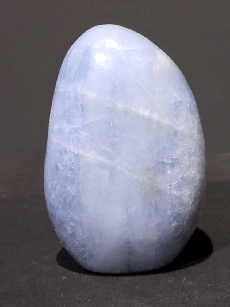 Blauwe calciet, 0,8kg, 12cm hoog, 24,- euro, nr. 23
Calciet is een veelvoorkomend mineraal dat voornamelijk bestaat uit calciumcarbonaat. Het komt in diverse kleuren en vormen voor en wordt in veel industrieën gebruikt, maar ook in de esoterie. 
Algemene kenmerken:
Samenstelling: Calciet bestaat voornamelijk uit calciumcarbonaat (CaCO3). 
Vorming: Het ontstaat door afzetting van calciumcarbonaat in water, maar ook door ophoping van schelpen en skeletten van zeedieren. 
Uiterlijk: Het heeft vaak een glasachtige glans, is doorzichtig tot doorschijnend en kan vele kleuren hebben, zoals geel, oranje, rood, bruin, blauw, groen, roze, wit en kleurloos. 
Hardheid: Calciet heeft een hardheid van 3 op de schaal van Mohs. 
Veelvoorkomend: Het is een van de meest voorkomende mineralen en is een hoofdbestanddeel van kalksteen, marmer en krijt. 
Esoterie:
In de edelsteentherapie wordt calciet gezien als een steen die energie versterkt, negatieve energieën verwijdert en spirituele groei bevordert. Verschillende kleuren calciet hebben specifieke eigenschappen, zoals gele calciet voor doorzettingsvermogen en moed, en mangano calciet voor emotionele heling. 
Specifieke calcietsoorten:
Gele Calciet: Staat bekend om het absorberen van negativiteit, het versterken van doorzettingsvermogen en het aantrekken van succes. 
Blauwe Calciet: Wordt geassocieerd met kalmering, communicatie en het loslaten van stress. 
Groene Calciet: Werkt op de hartchakra, bevordert liefde, compassie en emotionele heling. 
Mangano Calciet: Wordt gebruikt voor emotionele heling, het loslaten van oud verdriet en het versterken van zelfvertrouwen. 
Reiniging:
Calciet kan op verschillende manieren gereinigd worden, maar het is belangrijk om te weten dat sommige soorten, zoals gele calciet, niet goed tegen water kunnen. 
Andere reinigingsmethoden zijn bijvoorbeeld reinigen met edelstenenspray, op een Amethist of bergkristal leggen, of reinigen met selenite. 
Het is een steen die kan worden gebruikt voor energieversterking, emotionele heling en het bevorderen van spirituele groei, afhankelijk van de specifieke kleur en eigenschappen. 
                                                    -Kunstgalerie Arnold-