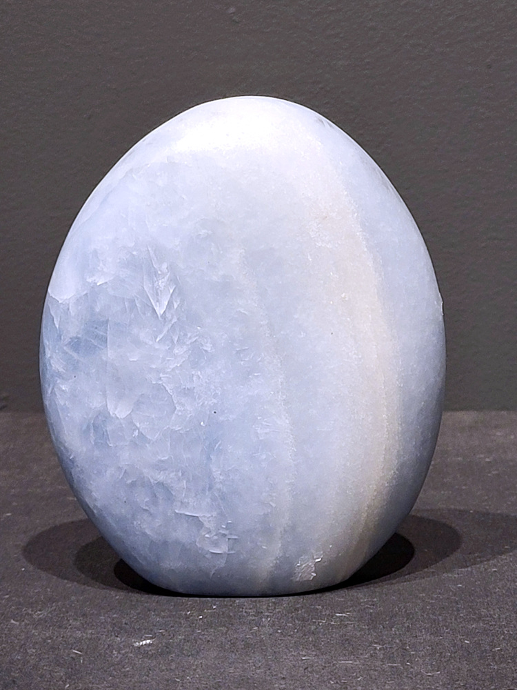 Blauwe calciet, 0,8kg, 12cm hoog, 25,- euro, nr. 24
Calciet is een veelvoorkomend mineraal dat voornamelijk bestaat uit calciumcarbonaat. Het komt in diverse kleuren en vormen voor en wordt in veel industrieën gebruikt, maar ook in de esoterie. 
Algemene kenmerken:
Samenstelling: Calciet bestaat voornamelijk uit calciumcarbonaat (CaCO3). 
Vorming: Het ontstaat door afzetting van calciumcarbonaat in water, maar ook door ophoping van schelpen en skeletten van zeedieren. 
Uiterlijk: Het heeft vaak een glasachtige glans, is doorzichtig tot doorschijnend en kan vele kleuren hebben, zoals geel, oranje, rood, bruin, blauw, groen, roze, wit en kleurloos. 
Hardheid: Calciet heeft een hardheid van 3 op de schaal van Mohs. 
Veelvoorkomend: Het is een van de meest voorkomende mineralen en is een hoofdbestanddeel van kalksteen, marmer en krijt. 
Esoterie:
In de edelsteentherapie wordt calciet gezien als een steen die energie versterkt, negatieve energieën verwijdert en spirituele groei bevordert. Verschillende kleuren calciet hebben specifieke eigenschappen, zoals gele calciet voor doorzettingsvermogen en moed, en mangano calciet voor emotionele heling. 
Specifieke calcietsoorten:
Gele Calciet: Staat bekend om het absorberen van negativiteit, het versterken van doorzettingsvermogen en het aantrekken van succes. 
Blauwe Calciet: Wordt geassocieerd met kalmering, communicatie en het loslaten van stress. 
Groene Calciet: Werkt op de hartchakra, bevordert liefde, compassie en emotionele heling. 
Mangano Calciet: Wordt gebruikt voor emotionele heling, het loslaten van oud verdriet en het versterken van zelfvertrouwen. 
Reiniging:
Calciet kan op verschillende manieren gereinigd worden, maar het is belangrijk om te weten dat sommige soorten, zoals gele calciet, niet goed tegen water kunnen. 
Andere reinigingsmethoden zijn bijvoorbeeld reinigen met edelstenenspray, op een Amethist of bergkristal leggen, of reinigen met selenite. 
Het is een steen die kan worden gebruikt voor energieversterking, emotionele heling en het bevorderen van spirituele groei, afhankelijk van de specifieke kleur en eigenschappen. 
                                                    -Kunstgalerie Arnold-