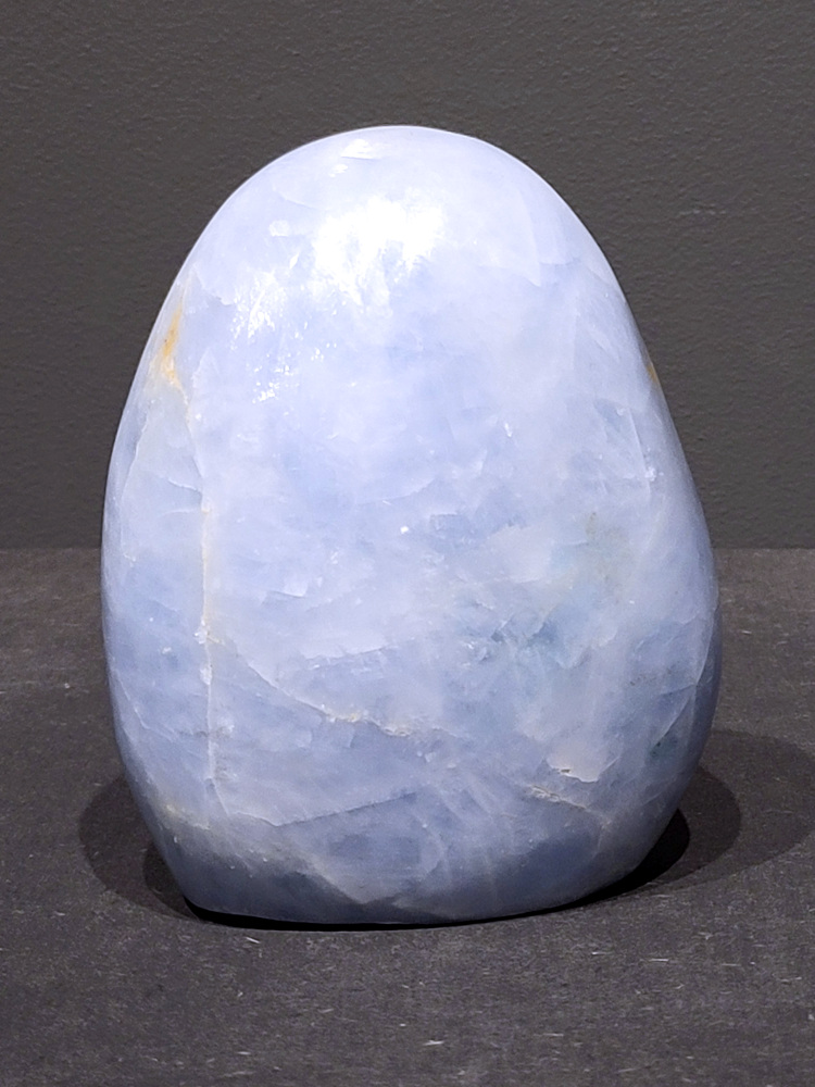 Blauwe calciet, 0,9kg, 11cm hoog, 28,- euro, nr. 27
Calciet is een veelvoorkomend mineraal dat voornamelijk bestaat uit calciumcarbonaat. Het komt in diverse kleuren en vormen voor en wordt in veel industrieën gebruikt, maar ook in de esoterie. 
Algemene kenmerken:
Samenstelling: Calciet bestaat voornamelijk uit calciumcarbonaat (CaCO3). 
Vorming: Het ontstaat door afzetting van calciumcarbonaat in water, maar ook door ophoping van schelpen en skeletten van zeedieren. 
Uiterlijk: Het heeft vaak een glasachtige glans, is doorzichtig tot doorschijnend en kan vele kleuren hebben, zoals geel, oranje, rood, bruin, blauw, groen, roze, wit en kleurloos. 
Hardheid: Calciet heeft een hardheid van 3 op de schaal van Mohs. 
Veelvoorkomend: Het is een van de meest voorkomende mineralen en is een hoofdbestanddeel van kalksteen, marmer en krijt. 
Esoterie:
In de edelsteentherapie wordt calciet gezien als een steen die energie versterkt, negatieve energieën verwijdert en spirituele groei bevordert. Verschillende kleuren calciet hebben specifieke eigenschappen, zoals gele calciet voor doorzettingsvermogen en moed, en mangano calciet voor emotionele heling. 
Specifieke calcietsoorten:
Gele Calciet: Staat bekend om het absorberen van negativiteit, het versterken van doorzettingsvermogen en het aantrekken van succes. 
Blauwe Calciet: Wordt geassocieerd met kalmering, communicatie en het loslaten van stress. 
Groene Calciet: Werkt op de hartchakra, bevordert liefde, compassie en emotionele heling. 
Mangano Calciet: Wordt gebruikt voor emotionele heling, het loslaten van oud verdriet en het versterken van zelfvertrouwen. 
Reiniging:
Calciet kan op verschillende manieren gereinigd worden, maar het is belangrijk om te weten dat sommige soorten, zoals gele calciet, niet goed tegen water kunnen. 
Andere reinigingsmethoden zijn bijvoorbeeld reinigen met edelstenenspray, op een Amethist of bergkristal leggen, of reinigen met selenite. 
Het is een steen die kan worden gebruikt voor energieversterking, emotionele heling en het bevorderen van spirituele groei, afhankelijk van de specifieke kleur en eigenschappen. 
                                                    -Kunstgalerie Arnold-