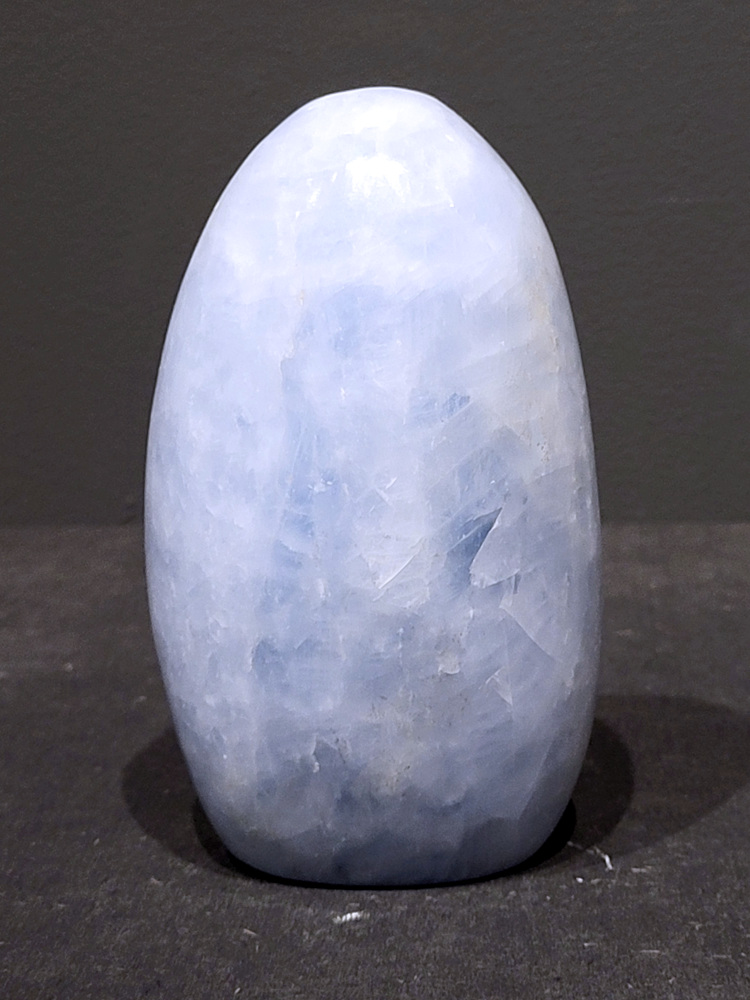 Blauwe calciet, 0,9kg, 12cm hoog, 27,- euro, nr. 29
Calciet is een veelvoorkomend mineraal dat voornamelijk bestaat uit calciumcarbonaat. Het komt in diverse kleuren en vormen voor en wordt in veel industrieën gebruikt, maar ook in de esoterie. 
Algemene kenmerken:
Samenstelling: Calciet bestaat voornamelijk uit calciumcarbonaat (CaCO3). 
Vorming: Het ontstaat door afzetting van calciumcarbonaat in water, maar ook door ophoping van schelpen en skeletten van zeedieren. 
Uiterlijk: Het heeft vaak een glasachtige glans, is doorzichtig tot doorschijnend en kan vele kleuren hebben, zoals geel, oranje, rood, bruin, blauw, groen, roze, wit en kleurloos. 
Hardheid: Calciet heeft een hardheid van 3 op de schaal van Mohs. 
Veelvoorkomend: Het is een van de meest voorkomende mineralen en is een hoofdbestanddeel van kalksteen, marmer en krijt. 
Esoterie:
In de edelsteentherapie wordt calciet gezien als een steen die energie versterkt, negatieve energieën verwijdert en spirituele groei bevordert. Verschillende kleuren calciet hebben specifieke eigenschappen, zoals gele calciet voor doorzettingsvermogen en moed, en mangano calciet voor emotionele heling. 
Specifieke calcietsoorten:
Gele Calciet: Staat bekend om het absorberen van negativiteit, het versterken van doorzettingsvermogen en het aantrekken van succes. 
Blauwe Calciet: Wordt geassocieerd met kalmering, communicatie en het loslaten van stress. 
Groene Calciet: Werkt op de hartchakra, bevordert liefde, compassie en emotionele heling. 
Mangano Calciet: Wordt gebruikt voor emotionele heling, het loslaten van oud verdriet en het versterken van zelfvertrouwen. 
Reiniging:
Calciet kan op verschillende manieren gereinigd worden, maar het is belangrijk om te weten dat sommige soorten, zoals gele calciet, niet goed tegen water kunnen. 
Andere reinigingsmethoden zijn bijvoorbeeld reinigen met edelstenenspray, op een Amethist of bergkristal leggen, of reinigen met selenite. 
Het is een steen die kan worden gebruikt voor energieversterking, emotionele heling en het bevorderen van spirituele groei, afhankelijk van de specifieke kleur en eigenschappen. 
                                                    -Kunstgalerie Arnold-