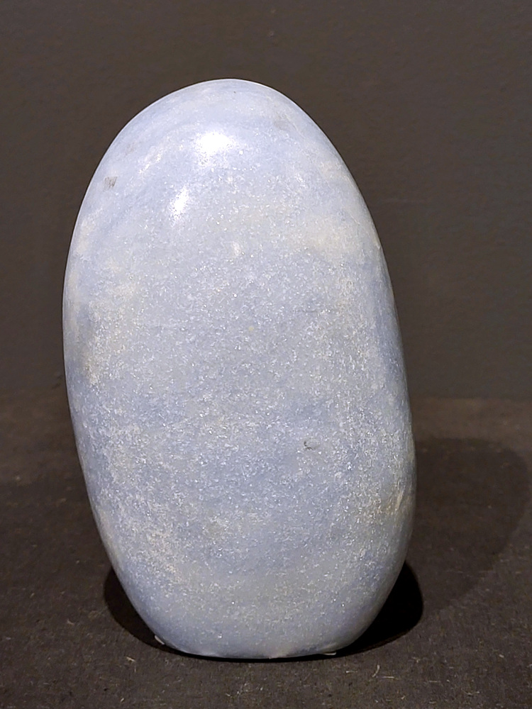 Blauwe calciet, 0,9kg, 13cm hoog, 26,- euro, nr. 31
Calciet is een veelvoorkomend mineraal dat voornamelijk bestaat uit calciumcarbonaat. Het komt in diverse kleuren en vormen voor en wordt in veel industrieën gebruikt, maar ook in de esoterie. 
Algemene kenmerken:
Samenstelling: Calciet bestaat voornamelijk uit calciumcarbonaat (CaCO3). 
Vorming: Het ontstaat door afzetting van calciumcarbonaat in water, maar ook door ophoping van schelpen en skeletten van zeedieren. 
Uiterlijk: Het heeft vaak een glasachtige glans, is doorzichtig tot doorschijnend en kan vele kleuren hebben, zoals geel, oranje, rood, bruin, blauw, groen, roze, wit en kleurloos. 
Hardheid: Calciet heeft een hardheid van 3 op de schaal van Mohs. 
Veelvoorkomend: Het is een van de meest voorkomende mineralen en is een hoofdbestanddeel van kalksteen, marmer en krijt. 
Esoterie:
In de edelsteentherapie wordt calciet gezien als een steen die energie versterkt, negatieve energieën verwijdert en spirituele groei bevordert. Verschillende kleuren calciet hebben specifieke eigenschappen, zoals gele calciet voor doorzettingsvermogen en moed, en mangano calciet voor emotionele heling. 
Specifieke calcietsoorten:
Gele Calciet: Staat bekend om het absorberen van negativiteit, het versterken van doorzettingsvermogen en het aantrekken van succes. 
Blauwe Calciet: Wordt geassocieerd met kalmering, communicatie en het loslaten van stress. 
Groene Calciet: Werkt op de hartchakra, bevordert liefde, compassie en emotionele heling. 
Mangano Calciet: Wordt gebruikt voor emotionele heling, het loslaten van oud verdriet en het versterken van zelfvertrouwen. 
Reiniging:
Calciet kan op verschillende manieren gereinigd worden, maar het is belangrijk om te weten dat sommige soorten, zoals gele calciet, niet goed tegen water kunnen. 
Andere reinigingsmethoden zijn bijvoorbeeld reinigen met edelstenenspray, op een Amethist of bergkristal leggen, of reinigen met selenite. 
Het is een steen die kan worden gebruikt voor energieversterking, emotionele heling en het bevorderen van spirituele groei, afhankelijk van de specifieke kleur en eigenschappen. 
                                                    -Kunstgalerie Arnold-