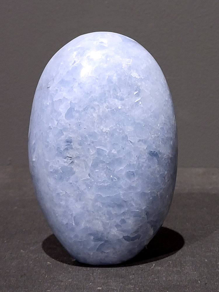 Blauwe calciet, 0,9kg, 13cm hoog, 28,- euro, nr. 32
Calciet is een veelvoorkomend mineraal dat voornamelijk bestaat uit calciumcarbonaat. Het komt in diverse kleuren en vormen voor en wordt in veel industrieën gebruikt, maar ook in de esoterie. 
Algemene kenmerken:
Samenstelling: Calciet bestaat voornamelijk uit calciumcarbonaat (CaCO3). 
Vorming: Het ontstaat door afzetting van calciumcarbonaat in water, maar ook door ophoping van schelpen en skeletten van zeedieren. 
Uiterlijk: Het heeft vaak een glasachtige glans, is doorzichtig tot doorschijnend en kan vele kleuren hebben, zoals geel, oranje, rood, bruin, blauw, groen, roze, wit en kleurloos. 
Hardheid: Calciet heeft een hardheid van 3 op de schaal van Mohs. 
Veelvoorkomend: Het is een van de meest voorkomende mineralen en is een hoofdbestanddeel van kalksteen, marmer en krijt. 
Esoterie:
In de edelsteentherapie wordt calciet gezien als een steen die energie versterkt, negatieve energieën verwijdert en spirituele groei bevordert. Verschillende kleuren calciet hebben specifieke eigenschappen, zoals gele calciet voor doorzettingsvermogen en moed, en mangano calciet voor emotionele heling. 
Specifieke calcietsoorten:
Gele Calciet: Staat bekend om het absorberen van negativiteit, het versterken van doorzettingsvermogen en het aantrekken van succes. 
Blauwe Calciet: Wordt geassocieerd met kalmering, communicatie en het loslaten van stress. 
Groene Calciet: Werkt op de hartchakra, bevordert liefde, compassie en emotionele heling. 
Mangano Calciet: Wordt gebruikt voor emotionele heling, het loslaten van oud verdriet en het versterken van zelfvertrouwen. 
Reiniging:
Calciet kan op verschillende manieren gereinigd worden, maar het is belangrijk om te weten dat sommige soorten, zoals gele calciet, niet goed tegen water kunnen. 
Andere reinigingsmethoden zijn bijvoorbeeld reinigen met edelstenenspray, op een Amethist of bergkristal leggen, of reinigen met selenite. 
Het is een steen die kan worden gebruikt voor energieversterking, emotionele heling en het bevorderen van spirituele groei, afhankelijk van de specifieke kleur en eigenschappen. 
                                                    -Kunstgalerie Arnold-