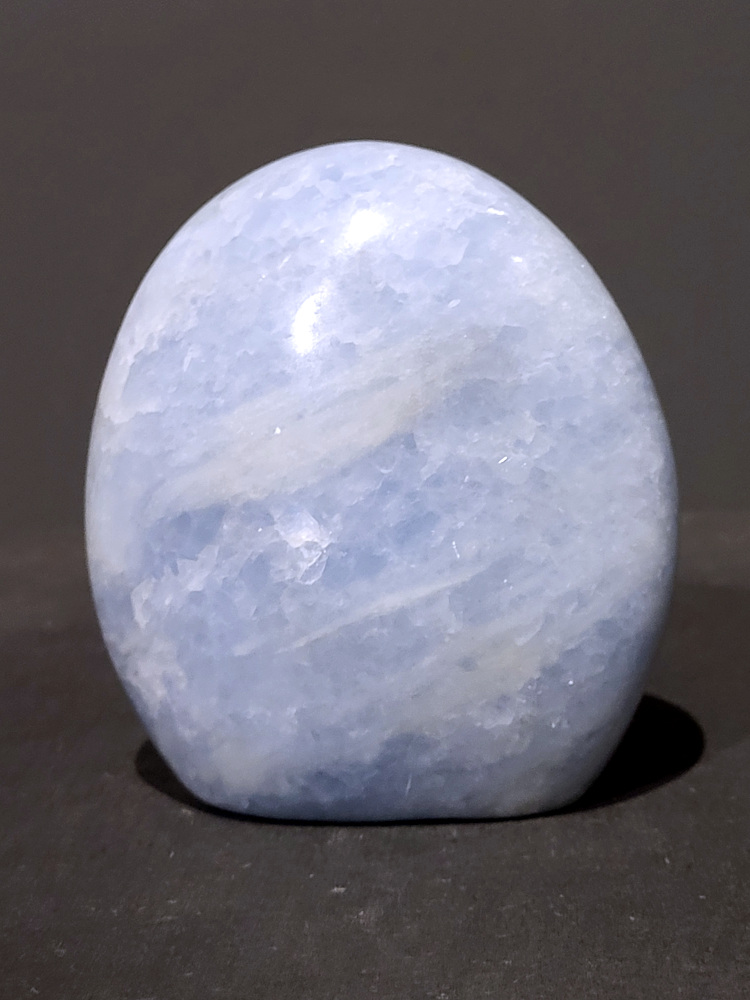 Blauwe calciet, 1,1kg, 11cm hoog, 32,- euro, nr. 33
Calciet is een veelvoorkomend mineraal dat voornamelijk bestaat uit calciumcarbonaat. Het komt in diverse kleuren en vormen voor en wordt in veel industrieën gebruikt, maar ook in de esoterie. 
Algemene kenmerken:
Samenstelling: Calciet bestaat voornamelijk uit calciumcarbonaat (CaCO3). 
Vorming: Het ontstaat door afzetting van calciumcarbonaat in water, maar ook door ophoping van schelpen en skeletten van zeedieren. 
Uiterlijk: Het heeft vaak een glasachtige glans, is doorzichtig tot doorschijnend en kan vele kleuren hebben, zoals geel, oranje, rood, bruin, blauw, groen, roze, wit en kleurloos. 
Hardheid: Calciet heeft een hardheid van 3 op de schaal van Mohs. 
Veelvoorkomend: Het is een van de meest voorkomende mineralen en is een hoofdbestanddeel van kalksteen, marmer en krijt. 
Esoterie:
In de edelsteentherapie wordt calciet gezien als een steen die energie versterkt, negatieve energieën verwijdert en spirituele groei bevordert. Verschillende kleuren calciet hebben specifieke eigenschappen, zoals gele calciet voor doorzettingsvermogen en moed, en mangano calciet voor emotionele heling. 
Specifieke calcietsoorten:
Gele Calciet: Staat bekend om het absorberen van negativiteit, het versterken van doorzettingsvermogen en het aantrekken van succes. 
Blauwe Calciet: Wordt geassocieerd met kalmering, communicatie en het loslaten van stress. 
Groene Calciet: Werkt op de hartchakra, bevordert liefde, compassie en emotionele heling. 
Mangano Calciet: Wordt gebruikt voor emotionele heling, het loslaten van oud verdriet en het versterken van zelfvertrouwen. 
Reiniging:
Calciet kan op verschillende manieren gereinigd worden, maar het is belangrijk om te weten dat sommige soorten, zoals gele calciet, niet goed tegen water kunnen. 
Andere reinigingsmethoden zijn bijvoorbeeld reinigen met edelstenenspray, op een Amethist of bergkristal leggen, of reinigen met selenite. 
Het is een steen die kan worden gebruikt voor energieversterking, emotionele heling en het bevorderen van spirituele groei, afhankelijk van de specifieke kleur en eigenschappen. 
                                                    -Kunstgalerie Arnold-