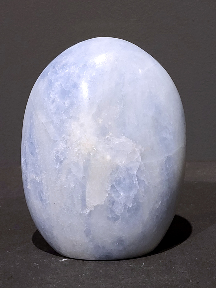 Blauwe calciet, 1,1kg, 12cm hoog, 34,- euro, nr. 33
Calciet is een veelvoorkomend mineraal dat voornamelijk bestaat uit calciumcarbonaat. Het komt in diverse kleuren en vormen voor en wordt in veel industrieën gebruikt, maar ook in de esoterie. 
Algemene kenmerken:
Samenstelling: Calciet bestaat voornamelijk uit calciumcarbonaat (CaCO3). 
Vorming: Het ontstaat door afzetting van calciumcarbonaat in water, maar ook door ophoping van schelpen en skeletten van zeedieren. 
Uiterlijk: Het heeft vaak een glasachtige glans, is doorzichtig tot doorschijnend en kan vele kleuren hebben, zoals geel, oranje, rood, bruin, blauw, groen, roze, wit en kleurloos. 
Hardheid: Calciet heeft een hardheid van 3 op de schaal van Mohs. 
Veelvoorkomend: Het is een van de meest voorkomende mineralen en is een hoofdbestanddeel van kalksteen, marmer en krijt. 
Esoterie:
In de edelsteentherapie wordt calciet gezien als een steen die energie versterkt, negatieve energieën verwijdert en spirituele groei bevordert. Verschillende kleuren calciet hebben specifieke eigenschappen, zoals gele calciet voor doorzettingsvermogen en moed, en mangano calciet voor emotionele heling. 
Specifieke calcietsoorten:
Gele Calciet: Staat bekend om het absorberen van negativiteit, het versterken van doorzettingsvermogen en het aantrekken van succes. 
Blauwe Calciet: Wordt geassocieerd met kalmering, communicatie en het loslaten van stress. 
Groene Calciet: Werkt op de hartchakra, bevordert liefde, compassie en emotionele heling. 
Mangano Calciet: Wordt gebruikt voor emotionele heling, het loslaten van oud verdriet en het versterken van zelfvertrouwen. 
Reiniging:
Calciet kan op verschillende manieren gereinigd worden, maar het is belangrijk om te weten dat sommige soorten, zoals gele calciet, niet goed tegen water kunnen. 
Andere reinigingsmethoden zijn bijvoorbeeld reinigen met edelstenenspray, op een Amethist of bergkristal leggen, of reinigen met selenite. 
Het is een steen die kan worden gebruikt voor energieversterking, emotionele heling en het bevorderen van spirituele groei, afhankelijk van de specifieke kleur en eigenschappen. 
                                                    -Kunstgalerie Arnold-