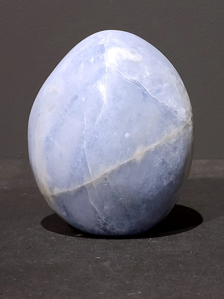 Blauwe calciet, 1,2kg, 12cm hoog, 36,- euro, nr. 34
Calciet is een veelvoorkomend mineraal dat voornamelijk bestaat uit calciumcarbonaat. Het komt in diverse kleuren en vormen voor en wordt in veel industrieën gebruikt, maar ook in de esoterie. 
Algemene kenmerken:
Samenstelling: Calciet bestaat voornamelijk uit calciumcarbonaat (CaCO3). 
Vorming: Het ontstaat door afzetting van calciumcarbonaat in water, maar ook door ophoping van schelpen en skeletten van zeedieren. 
Uiterlijk: Het heeft vaak een glasachtige glans, is doorzichtig tot doorschijnend en kan vele kleuren hebben, zoals geel, oranje, rood, bruin, blauw, groen, roze, wit en kleurloos. 
Hardheid: Calciet heeft een hardheid van 3 op de schaal van Mohs. 
Veelvoorkomend: Het is een van de meest voorkomende mineralen en is een hoofdbestanddeel van kalksteen, marmer en krijt. 
Esoterie:
In de edelsteentherapie wordt calciet gezien als een steen die energie versterkt, negatieve energieën verwijdert en spirituele groei bevordert. Verschillende kleuren calciet hebben specifieke eigenschappen, zoals gele calciet voor doorzettingsvermogen en moed, en mangano calciet voor emotionele heling. 
Specifieke calcietsoorten:
Gele Calciet: Staat bekend om het absorberen van negativiteit, het versterken van doorzettingsvermogen en het aantrekken van succes. 
Blauwe Calciet: Wordt geassocieerd met kalmering, communicatie en het loslaten van stress. 
Groene Calciet: Werkt op de hartchakra, bevordert liefde, compassie en emotionele heling. 
Mangano Calciet: Wordt gebruikt voor emotionele heling, het loslaten van oud verdriet en het versterken van zelfvertrouwen. 
Reiniging:
Calciet kan op verschillende manieren gereinigd worden, maar het is belangrijk om te weten dat sommige soorten, zoals gele calciet, niet goed tegen water kunnen. 
Andere reinigingsmethoden zijn bijvoorbeeld reinigen met edelstenenspray, op een Amethist of bergkristal leggen, of reinigen met selenite. 
Het is een steen die kan worden gebruikt voor energieversterking, emotionele heling en het bevorderen van spirituele groei, afhankelijk van de specifieke kleur en eigenschappen. 
                                                    -Kunstgalerie Arnold-