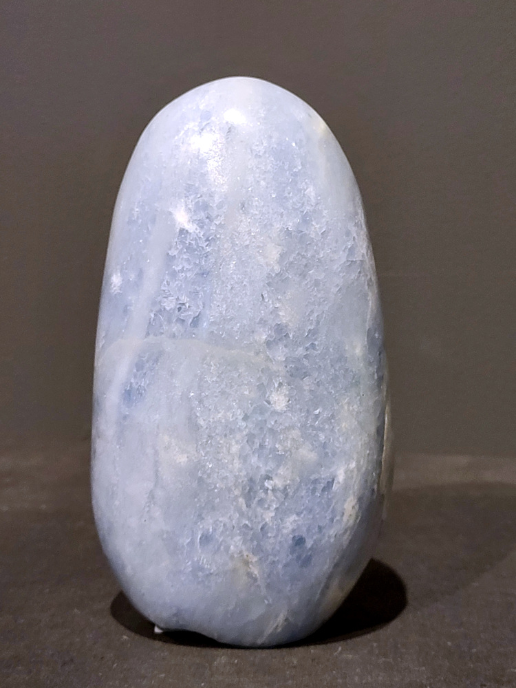 Blauwe calciet, 1,2kg, 14cm hoog, 36,- euro, nr. 35
Calciet is een veelvoorkomend mineraal dat voornamelijk bestaat uit calciumcarbonaat. Het komt in diverse kleuren en vormen voor en wordt in veel industrieën gebruikt, maar ook in de esoterie. 
Algemene kenmerken:
Samenstelling: Calciet bestaat voornamelijk uit calciumcarbonaat (CaCO3). 
Vorming: Het ontstaat door afzetting van calciumcarbonaat in water, maar ook door ophoping van schelpen en skeletten van zeedieren. 
Uiterlijk: Het heeft vaak een glasachtige glans, is doorzichtig tot doorschijnend en kan vele kleuren hebben, zoals geel, oranje, rood, bruin, blauw, groen, roze, wit en kleurloos. 
Hardheid: Calciet heeft een hardheid van 3 op de schaal van Mohs. 
Veelvoorkomend: Het is een van de meest voorkomende mineralen en is een hoofdbestanddeel van kalksteen, marmer en krijt. 
Esoterie:
In de edelsteentherapie wordt calciet gezien als een steen die energie versterkt, negatieve energieën verwijdert en spirituele groei bevordert. Verschillende kleuren calciet hebben specifieke eigenschappen, zoals gele calciet voor doorzettingsvermogen en moed, en mangano calciet voor emotionele heling. 
Specifieke calcietsoorten:
Gele Calciet: Staat bekend om het absorberen van negativiteit, het versterken van doorzettingsvermogen en het aantrekken van succes. 
Blauwe Calciet: Wordt geassocieerd met kalmering, communicatie en het loslaten van stress. 
Groene Calciet: Werkt op de hartchakra, bevordert liefde, compassie en emotionele heling. 
Mangano Calciet: Wordt gebruikt voor emotionele heling, het loslaten van oud verdriet en het versterken van zelfvertrouwen. 
Reiniging:
Calciet kan op verschillende manieren gereinigd worden, maar het is belangrijk om te weten dat sommige soorten, zoals gele calciet, niet goed tegen water kunnen. 
Andere reinigingsmethoden zijn bijvoorbeeld reinigen met edelstenenspray, op een Amethist of bergkristal leggen, of reinigen met selenite. 
Het is een steen die kan worden gebruikt voor energieversterking, emotionele heling en het bevorderen van spirituele groei, afhankelijk van de specifieke kleur en eigenschappen. 
                                                    -Kunstgalerie Arnold-