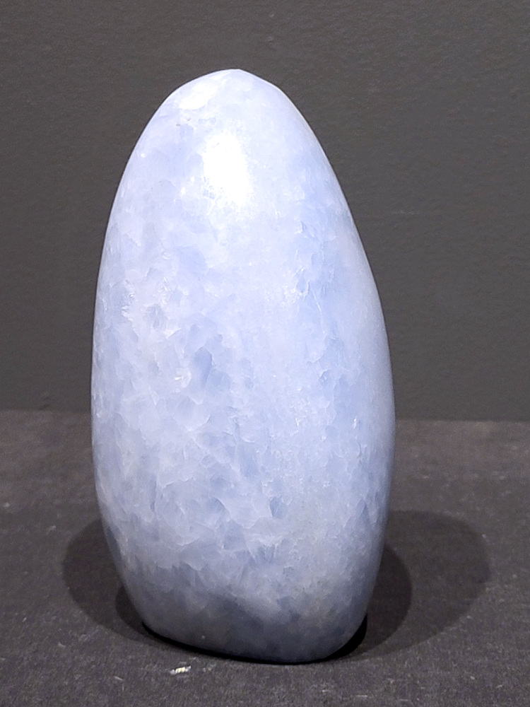 Blauwe calciet, 1,3kg, 15cm hoog, 39,- euro, nr. 9
Calciet is een veelvoorkomend mineraal dat voornamelijk bestaat uit calciumcarbonaat. Het komt in diverse kleuren en vormen voor en wordt in veel industrieën gebruikt, maar ook in de esoterie. 
Algemene kenmerken:
Samenstelling: Calciet bestaat voornamelijk uit calciumcarbonaat (CaCO3). 
Vorming: Het ontstaat door afzetting van calciumcarbonaat in water, maar ook door ophoping van schelpen en skeletten van zeedieren. 
Uiterlijk: Het heeft vaak een glasachtige glans, is doorzichtig tot doorschijnend en kan vele kleuren hebben, zoals geel, oranje, rood, bruin, blauw, groen, roze, wit en kleurloos. 
Hardheid: Calciet heeft een hardheid van 3 op de schaal van Mohs. 
Veelvoorkomend: Het is een van de meest voorkomende mineralen en is een hoofdbestanddeel van kalksteen, marmer en krijt. 
Esoterie:
In de edelsteentherapie wordt calciet gezien als een steen die energie versterkt, negatieve energieën verwijdert en spirituele groei bevordert. Verschillende kleuren calciet hebben specifieke eigenschappen, zoals gele calciet voor doorzettingsvermogen en moed, en mangano calciet voor emotionele heling. 
Specifieke calcietsoorten:
Gele Calciet: Staat bekend om het absorberen van negativiteit, het versterken van doorzettingsvermogen en het aantrekken van succes. 
Blauwe Calciet: Wordt geassocieerd met kalmering, communicatie en het loslaten van stress. 
Groene Calciet: Werkt op de hartchakra, bevordert liefde, compassie en emotionele heling. 
Mangano Calciet: Wordt gebruikt voor emotionele heling, het loslaten van oud verdriet en het versterken van zelfvertrouwen. 
Reiniging:
Calciet kan op verschillende manieren gereinigd worden, maar het is belangrijk om te weten dat sommige soorten, zoals gele calciet, niet goed tegen water kunnen. 
Andere reinigingsmethoden zijn bijvoorbeeld reinigen met edelstenenspray, op een Amethist of bergkristal leggen, of reinigen met selenite. 
Het is een steen die kan worden gebruikt voor energieversterking, emotionele heling en het bevorderen van spirituele groei, afhankelijk van de specifieke kleur en eigenschappen. 
                                                    -Kunstgalerie Arnold-