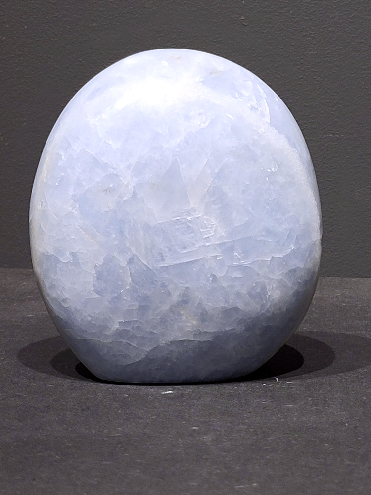 Blauwe calciet, 1,5kg, 13cm hoog, 45,- euro, nr. 36
Calciet is een veelvoorkomend mineraal dat voornamelijk bestaat uit calciumcarbonaat. Het komt in diverse kleuren en vormen voor en wordt in veel industrieën gebruikt, maar ook in de esoterie. 
Algemene kenmerken:
Samenstelling: Calciet bestaat voornamelijk uit calciumcarbonaat (CaCO3). 
Vorming: Het ontstaat door afzetting van calciumcarbonaat in water, maar ook door ophoping van schelpen en skeletten van zeedieren. 
Uiterlijk: Het heeft vaak een glasachtige glans, is doorzichtig tot doorschijnend en kan vele kleuren hebben, zoals geel, oranje, rood, bruin, blauw, groen, roze, wit en kleurloos. 
Hardheid: Calciet heeft een hardheid van 3 op de schaal van Mohs. 
Veelvoorkomend: Het is een van de meest voorkomende mineralen en is een hoofdbestanddeel van kalksteen, marmer en krijt. 
Esoterie:
In de edelsteentherapie wordt calciet gezien als een steen die energie versterkt, negatieve energieën verwijdert en spirituele groei bevordert. Verschillende kleuren calciet hebben specifieke eigenschappen, zoals gele calciet voor doorzettingsvermogen en moed, en mangano calciet voor emotionele heling. 
Specifieke calcietsoorten:
Gele Calciet: Staat bekend om het absorberen van negativiteit, het versterken van doorzettingsvermogen en het aantrekken van succes. 
Blauwe Calciet: Wordt geassocieerd met kalmering, communicatie en het loslaten van stress. 
Groene Calciet: Werkt op de hartchakra, bevordert liefde, compassie en emotionele heling. 
Mangano Calciet: Wordt gebruikt voor emotionele heling, het loslaten van oud verdriet en het versterken van zelfvertrouwen. 
Reiniging:
Calciet kan op verschillende manieren gereinigd worden, maar het is belangrijk om te weten dat sommige soorten, zoals gele calciet, niet goed tegen water kunnen. 
Andere reinigingsmethoden zijn bijvoorbeeld reinigen met edelstenenspray, op een Amethist of bergkristal leggen, of reinigen met selenite. 
Het is een steen die kan worden gebruikt voor energieversterking, emotionele heling en het bevorderen van spirituele groei, afhankelijk van de specifieke kleur en eigenschappen. 
                                                    -Kunstgalerie Arnold-