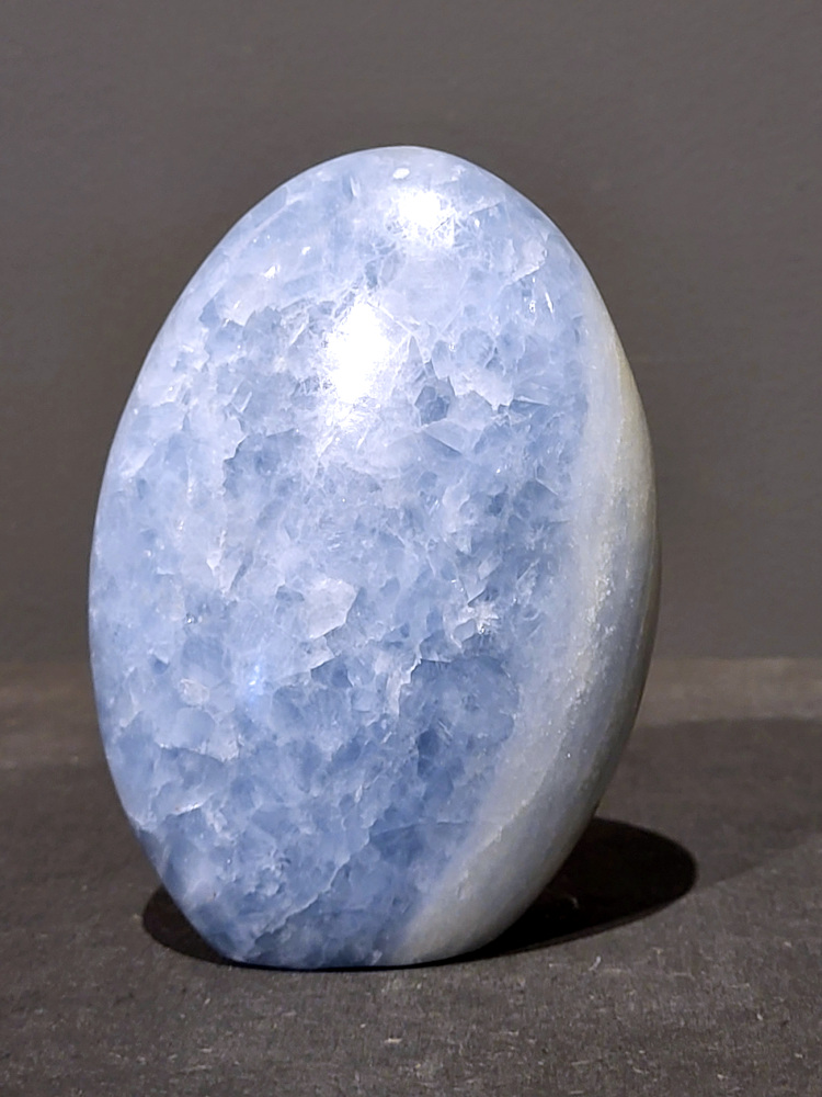 Blauwe calciet, 1kg, 12cm hoog, 29,- euro, nr. 37
Calciet is een veelvoorkomend mineraal dat voornamelijk bestaat uit calciumcarbonaat. Het komt in diverse kleuren en vormen voor en wordt in veel industrieën gebruikt, maar ook in de esoterie. 
Algemene kenmerken:
Samenstelling: Calciet bestaat voornamelijk uit calciumcarbonaat (CaCO3). 
Vorming: Het ontstaat door afzetting van calciumcarbonaat in water, maar ook door ophoping van schelpen en skeletten van zeedieren. 
Uiterlijk: Het heeft vaak een glasachtige glans, is doorzichtig tot doorschijnend en kan vele kleuren hebben, zoals geel, oranje, rood, bruin, blauw, groen, roze, wit en kleurloos. 
Hardheid: Calciet heeft een hardheid van 3 op de schaal van Mohs. 
Veelvoorkomend: Het is een van de meest voorkomende mineralen en is een hoofdbestanddeel van kalksteen, marmer en krijt. 
Esoterie:
In de edelsteentherapie wordt calciet gezien als een steen die energie versterkt, negatieve energieën verwijdert en spirituele groei bevordert. Verschillende kleuren calciet hebben specifieke eigenschappen, zoals gele calciet voor doorzettingsvermogen en moed, en mangano calciet voor emotionele heling. 
Specifieke calcietsoorten:
Gele Calciet: Staat bekend om het absorberen van negativiteit, het versterken van doorzettingsvermogen en het aantrekken van succes. 
Blauwe Calciet: Wordt geassocieerd met kalmering, communicatie en het loslaten van stress. 
Groene Calciet: Werkt op de hartchakra, bevordert liefde, compassie en emotionele heling. 
Mangano Calciet: Wordt gebruikt voor emotionele heling, het loslaten van oud verdriet en het versterken van zelfvertrouwen. 
Reiniging:
Calciet kan op verschillende manieren gereinigd worden, maar het is belangrijk om te weten dat sommige soorten, zoals gele calciet, niet goed tegen water kunnen. 
Andere reinigingsmethoden zijn bijvoorbeeld reinigen met edelstenenspray, op een Amethist of bergkristal leggen, of reinigen met selenite. 
Het is een steen die kan worden gebruikt voor energieversterking, emotionele heling en het bevorderen van spirituele groei, afhankelijk van de specifieke kleur en eigenschappen. 
                                                    -Kunstgalerie Arnold-