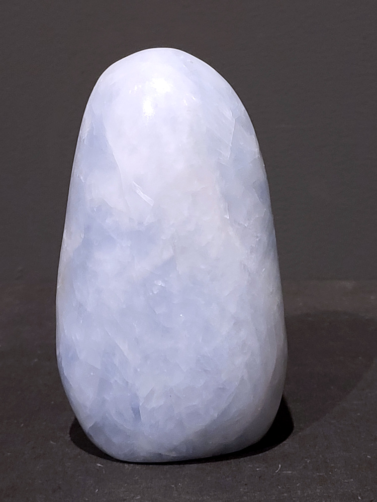 Blauwe calciet, 1kg, 13cm hoog, 29,- euro, nr. 38
Calciet is een veelvoorkomend mineraal dat voornamelijk bestaat uit calciumcarbonaat. Het komt in diverse kleuren en vormen voor en wordt in veel industrieën gebruikt, maar ook in de esoterie. 
Algemene kenmerken:
Samenstelling: Calciet bestaat voornamelijk uit calciumcarbonaat (CaCO3). 
Vorming: Het ontstaat door afzetting van calciumcarbonaat in water, maar ook door ophoping van schelpen en skeletten van zeedieren. 
Uiterlijk: Het heeft vaak een glasachtige glans, is doorzichtig tot doorschijnend en kan vele kleuren hebben, zoals geel, oranje, rood, bruin, blauw, groen, roze, wit en kleurloos. 
Hardheid: Calciet heeft een hardheid van 3 op de schaal van Mohs. 
Veelvoorkomend: Het is een van de meest voorkomende mineralen en is een hoofdbestanddeel van kalksteen, marmer en krijt. 
Esoterie:
In de edelsteentherapie wordt calciet gezien als een steen die energie versterkt, negatieve energieën verwijdert en spirituele groei bevordert. Verschillende kleuren calciet hebben specifieke eigenschappen, zoals gele calciet voor doorzettingsvermogen en moed, en mangano calciet voor emotionele heling. 
Specifieke calcietsoorten:
Gele Calciet: Staat bekend om het absorberen van negativiteit, het versterken van doorzettingsvermogen en het aantrekken van succes. 
Blauwe Calciet: Wordt geassocieerd met kalmering, communicatie en het loslaten van stress. 
Groene Calciet: Werkt op de hartchakra, bevordert liefde, compassie en emotionele heling. 
Mangano Calciet: Wordt gebruikt voor emotionele heling, het loslaten van oud verdriet en het versterken van zelfvertrouwen. 
Reiniging:
Calciet kan op verschillende manieren gereinigd worden, maar het is belangrijk om te weten dat sommige soorten, zoals gele calciet, niet goed tegen water kunnen. 
Andere reinigingsmethoden zijn bijvoorbeeld reinigen met edelstenenspray, op een Amethist of bergkristal leggen, of reinigen met selenite. 
Het is een steen die kan worden gebruikt voor energieversterking, emotionele heling en het bevorderen van spirituele groei, afhankelijk van de specifieke kleur en eigenschappen. 
                                                    -Kunstgalerie Arnold-