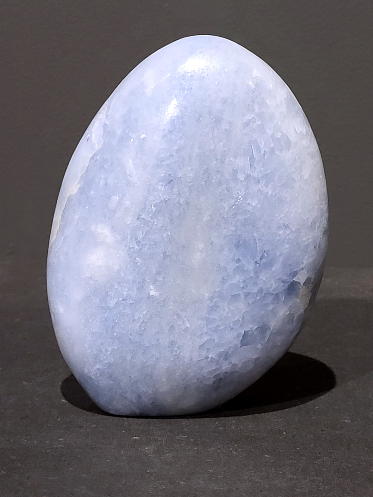 Blauwe calciet, 1kg, 14cm hoog, 31,- euro, nr. 39
Calciet is een veelvoorkomend mineraal dat voornamelijk bestaat uit calciumcarbonaat. Het komt in diverse kleuren en vormen voor en wordt in veel industrieën gebruikt, maar ook in de esoterie. 
Algemene kenmerken:
Samenstelling: Calciet bestaat voornamelijk uit calciumcarbonaat (CaCO3). 
Vorming: Het ontstaat door afzetting van calciumcarbonaat in water, maar ook door ophoping van schelpen en skeletten van zeedieren. 
Uiterlijk: Het heeft vaak een glasachtige glans, is doorzichtig tot doorschijnend en kan vele kleuren hebben, zoals geel, oranje, rood, bruin, blauw, groen, roze, wit en kleurloos. 
Hardheid: Calciet heeft een hardheid van 3 op de schaal van Mohs. 
Veelvoorkomend: Het is een van de meest voorkomende mineralen en is een hoofdbestanddeel van kalksteen, marmer en krijt. 
Esoterie:
In de edelsteentherapie wordt calciet gezien als een steen die energie versterkt, negatieve energieën verwijdert en spirituele groei bevordert. Verschillende kleuren calciet hebben specifieke eigenschappen, zoals gele calciet voor doorzettingsvermogen en moed, en mangano calciet voor emotionele heling. 
Specifieke calcietsoorten:
Gele Calciet: Staat bekend om het absorberen van negativiteit, het versterken van doorzettingsvermogen en het aantrekken van succes. 
Blauwe Calciet: Wordt geassocieerd met kalmering, communicatie en het loslaten van stress. 
Groene Calciet: Werkt op de hartchakra, bevordert liefde, compassie en emotionele heling. 
Mangano Calciet: Wordt gebruikt voor emotionele heling, het loslaten van oud verdriet en het versterken van zelfvertrouwen. 
Reiniging:
Calciet kan op verschillende manieren gereinigd worden, maar het is belangrijk om te weten dat sommige soorten, zoals gele calciet, niet goed tegen water kunnen. 
Andere reinigingsmethoden zijn bijvoorbeeld reinigen met edelstenenspray, op een Amethist of bergkristal leggen, of reinigen met selenite. 
Het is een steen die kan worden gebruikt voor energieversterking, emotionele heling en het bevorderen van spirituele groei, afhankelijk van de specifieke kleur en eigenschappen. 
                                                    -Kunstgalerie Arnold-