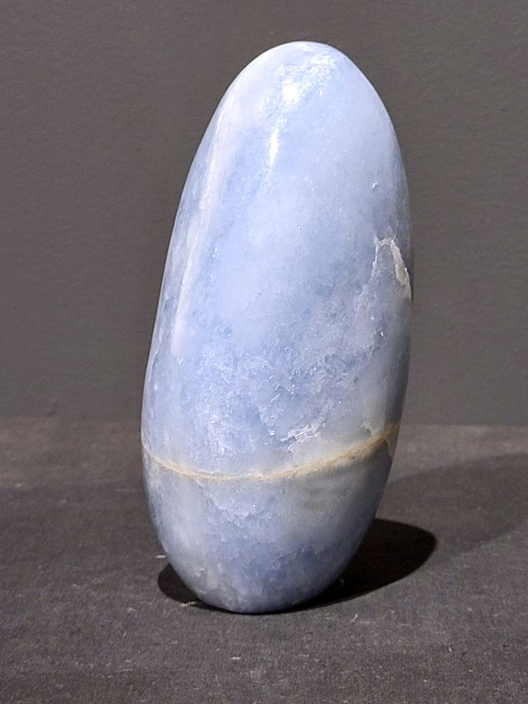 Blauwe calciet, 1kg, 14cm hoog, 31,- euro, nr. 40
Calciet is een veelvoorkomend mineraal dat voornamelijk bestaat uit calciumcarbonaat. Het komt in diverse kleuren en vormen voor en wordt in veel industrieën gebruikt, maar ook in de esoterie. 
Algemene kenmerken:
Samenstelling: Calciet bestaat voornamelijk uit calciumcarbonaat (CaCO3). 
Vorming: Het ontstaat door afzetting van calciumcarbonaat in water, maar ook door ophoping van schelpen en skeletten van zeedieren. 
Uiterlijk: Het heeft vaak een glasachtige glans, is doorzichtig tot doorschijnend en kan vele kleuren hebben, zoals geel, oranje, rood, bruin, blauw, groen, roze, wit en kleurloos. 
Hardheid: Calciet heeft een hardheid van 3 op de schaal van Mohs. 
Veelvoorkomend: Het is een van de meest voorkomende mineralen en is een hoofdbestanddeel van kalksteen, marmer en krijt. 
Esoterie:
In de edelsteentherapie wordt calciet gezien als een steen die energie versterkt, negatieve energieën verwijdert en spirituele groei bevordert. Verschillende kleuren calciet hebben specifieke eigenschappen, zoals gele calciet voor doorzettingsvermogen en moed, en mangano calciet voor emotionele heling. 
Specifieke calcietsoorten:
Gele Calciet: Staat bekend om het absorberen van negativiteit, het versterken van doorzettingsvermogen en het aantrekken van succes. 
Blauwe Calciet: Wordt geassocieerd met kalmering, communicatie en het loslaten van stress. 
Groene Calciet: Werkt op de hartchakra, bevordert liefde, compassie en emotionele heling. 
Mangano Calciet: Wordt gebruikt voor emotionele heling, het loslaten van oud verdriet en het versterken van zelfvertrouwen. 
Reiniging:
Calciet kan op verschillende manieren gereinigd worden, maar het is belangrijk om te weten dat sommige soorten, zoals gele calciet, niet goed tegen water kunnen. 
Andere reinigingsmethoden zijn bijvoorbeeld reinigen met edelstenenspray, op een Amethist of bergkristal leggen, of reinigen met selenite. 
Het is een steen die kan worden gebruikt voor energieversterking, emotionele heling en het bevorderen van spirituele groei, afhankelijk van de specifieke kleur en eigenschappen. 
                                                    -Kunstgalerie Arnold-