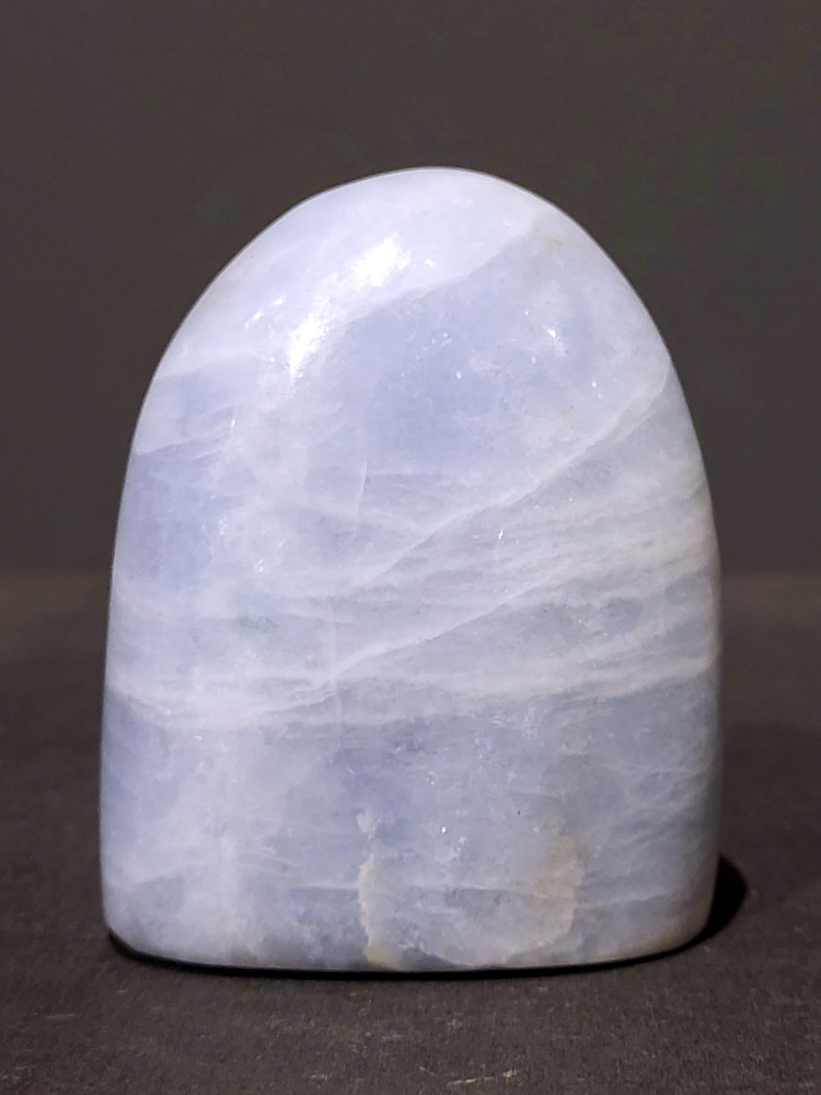 Blauwe calciet, sculptuur, 0,5kg, 9cm hoog, 16,-euro, nr. 41
Calciet is een veelvoorkomend mineraal dat voornamelijk bestaat uit calciumcarbonaat. Het komt in diverse kleuren en vormen voor en wordt in veel industrieën gebruikt, maar ook in de esoterie. 
Algemene kenmerken:
Samenstelling: Calciet bestaat voornamelijk uit calciumcarbonaat (CaCO3). 
Vorming: Het ontstaat door afzetting van calciumcarbonaat in water, maar ook door ophoping van schelpen en skeletten van zeedieren. 
Uiterlijk: Het heeft vaak een glasachtige glans, is doorzichtig tot doorschijnend en kan vele kleuren hebben, zoals geel, oranje, rood, bruin, blauw, groen, roze, wit en kleurloos. 
Hardheid: Calciet heeft een hardheid van 3 op de schaal van Mohs. 
Veelvoorkomend: Het is een van de meest voorkomende mineralen en is een hoofdbestanddeel van kalksteen, marmer en krijt. 
Esoterie:
In de edelsteentherapie wordt calciet gezien als een steen die energie versterkt, negatieve energieën verwijdert en spirituele groei bevordert. Verschillende kleuren calciet hebben specifieke eigenschappen, zoals gele calciet voor doorzettingsvermogen en moed, en mangano calciet voor emotionele heling. 
Specifieke calcietsoorten:
Gele Calciet: Staat bekend om het absorberen van negativiteit, het versterken van doorzettingsvermogen en het aantrekken van succes. 
Blauwe Calciet: Wordt geassocieerd met kalmering, communicatie en het loslaten van stress. 
Groene Calciet: Werkt op de hartchakra, bevordert liefde, compassie en emotionele heling. 
Mangano Calciet: Wordt gebruikt voor emotionele heling, het loslaten van oud verdriet en het versterken van zelfvertrouwen. 
Reiniging:
Calciet kan op verschillende manieren gereinigd worden, maar het is belangrijk om te weten dat sommige soorten, zoals gele calciet, niet goed tegen water kunnen. 
Andere reinigingsmethoden zijn bijvoorbeeld reinigen met edelstenenspray, op een Amethist of bergkristal leggen, of reinigen met selenite. 
Het is een steen die kan worden gebruikt voor energieversterking, emotionele heling en het bevorderen van spirituele groei, afhankelijk van de specifieke kleur en eigenschappen. 
                                                    -Kunstgalerie Arnold-