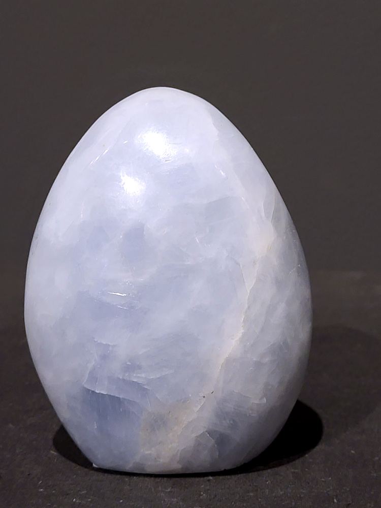 Blauwe calciet, sculptuur, 0,7kg, 10cm hoog, 21,- euro, nr. 42
Calciet is een veelvoorkomend mineraal dat voornamelijk bestaat uit calciumcarbonaat. Het komt in diverse kleuren en vormen voor en wordt in veel industrieën gebruikt, maar ook in de esoterie. 
Algemene kenmerken:
Samenstelling: Calciet bestaat voornamelijk uit calciumcarbonaat (CaCO3). 
Vorming: Het ontstaat door afzetting van calciumcarbonaat in water, maar ook door ophoping van schelpen en skeletten van zeedieren. 
Uiterlijk: Het heeft vaak een glasachtige glans, is doorzichtig tot doorschijnend en kan vele kleuren hebben, zoals geel, oranje, rood, bruin, blauw, groen, roze, wit en kleurloos. 
Hardheid: Calciet heeft een hardheid van 3 op de schaal van Mohs. 
Veelvoorkomend: Het is een van de meest voorkomende mineralen en is een hoofdbestanddeel van kalksteen, marmer en krijt. 
Esoterie:
In de edelsteentherapie wordt calciet gezien als een steen die energie versterkt, negatieve energieën verwijdert en spirituele groei bevordert. Verschillende kleuren calciet hebben specifieke eigenschappen, zoals gele calciet voor doorzettingsvermogen en moed, en mangano calciet voor emotionele heling. 
Specifieke calcietsoorten:
Gele Calciet: Staat bekend om het absorberen van negativiteit, het versterken van doorzettingsvermogen en het aantrekken van succes. 
Blauwe Calciet: Wordt geassocieerd met kalmering, communicatie en het loslaten van stress. 
Groene Calciet: Werkt op de hartchakra, bevordert liefde, compassie en emotionele heling. 
Mangano Calciet: Wordt gebruikt voor emotionele heling, het loslaten van oud verdriet en het versterken van zelfvertrouwen. 
Reiniging:
Calciet kan op verschillende manieren gereinigd worden, maar het is belangrijk om te weten dat sommige soorten, zoals gele calciet, niet goed tegen water kunnen. 
Andere reinigingsmethoden zijn bijvoorbeeld reinigen met edelstenenspray, op een Amethist of bergkristal leggen, of reinigen met selenite. 
Het is een steen die kan worden gebruikt voor energieversterking, emotionele heling en het bevorderen van spirituele groei, afhankelijk van de specifieke kleur en eigenschappen. 
                                                    -Kunstgalerie Arnold-