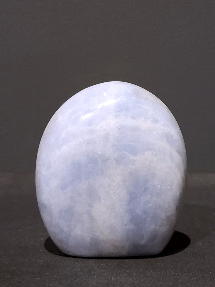 Blauwe calciet, sculptuur, 0,8kg, 11cm hoog, 23,- euro, nr. 43
Calciet is een veelvoorkomend mineraal dat voornamelijk bestaat uit calciumcarbonaat. Het komt in diverse kleuren en vormen voor en wordt in veel industrieën gebruikt, maar ook in de esoterie. 
Algemene kenmerken:
Samenstelling: Calciet bestaat voornamelijk uit calciumcarbonaat (CaCO3). 
Vorming: Het ontstaat door afzetting van calciumcarbonaat in water, maar ook door ophoping van schelpen en skeletten van zeedieren. 
Uiterlijk: Het heeft vaak een glasachtige glans, is doorzichtig tot doorschijnend en kan vele kleuren hebben, zoals geel, oranje, rood, bruin, blauw, groen, roze, wit en kleurloos. 
Hardheid: Calciet heeft een hardheid van 3 op de schaal van Mohs. 
Veelvoorkomend: Het is een van de meest voorkomende mineralen en is een hoofdbestanddeel van kalksteen, marmer en krijt. 
Esoterie:
In de edelsteentherapie wordt calciet gezien als een steen die energie versterkt, negatieve energieën verwijdert en spirituele groei bevordert. Verschillende kleuren calciet hebben specifieke eigenschappen, zoals gele calciet voor doorzettingsvermogen en moed, en mangano calciet voor emotionele heling. 
Specifieke calcietsoorten:
Gele Calciet: Staat bekend om het absorberen van negativiteit, het versterken van doorzettingsvermogen en het aantrekken van succes. 
Blauwe Calciet: Wordt geassocieerd met kalmering, communicatie en het loslaten van stress. 
Groene Calciet: Werkt op de hartchakra, bevordert liefde, compassie en emotionele heling. 
Mangano Calciet: Wordt gebruikt voor emotionele heling, het loslaten van oud verdriet en het versterken van zelfvertrouwen. 
Reiniging:
Calciet kan op verschillende manieren gereinigd worden, maar het is belangrijk om te weten dat sommige soorten, zoals gele calciet, niet goed tegen water kunnen. 
Andere reinigingsmethoden zijn bijvoorbeeld reinigen met edelstenenspray, op een Amethist of bergkristal leggen, of reinigen met selenite. 
Het is een steen die kan worden gebruikt voor energieversterking, emotionele heling en het bevorderen van spirituele groei, afhankelijk van de specifieke kleur en eigenschappen. 
                                                    -Kunstgalerie Arnold-