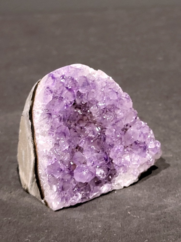 Amethist druzy, 0,2kg, 8,- euro, nr. 4.

Beschrijving Amethist.
Amethist is een paarse variëteit van kwarts, bekend om zijn kalmerende en spirituele eigenschappen. De kleur varieert van licht lila tot diep violet en wordt veroorzaakt door sporen van ijzer en andere elementen. Amethist wordt al eeuwenlang gewaardeerd, zowel vanwege zijn esthetische schoonheid als zijn vermeende genezende en beschermende krachten. 
Amethist is een kwartskristal, vaak te vinden in geodes (holtes in gesteente) of als afzonderlijke kristallen. 
De kleur varieert van lichtpaars tot diep violet, soms met roze of blauwe tinten. 
De kleurintensiteit kan variëren, waarbij donkerdere amethisten vaak als kwalitatief worden beschouwd. 
Soms vertoont amethist dichroïsme, waarbij je verschillende kleuren kunt zien wanneer je de steen in het licht draait. 

Vindplaatsen:
Amethist wordt gevonden in verschillende delen van de wereld, waaronder Brazilië, Uruguay, Zambia, Madagaskar, Rusland en Canada.
Het wordt vaak gevonden in bergachtige gebieden. 

Gebruik:
Amethist wordt gebruikt in sieraden, decoratieve objecten en als helende steen. 
Het wordt vaak gedragen als hanger, ring of armband, of geplaatst in ruimtes om de energie te zuiveren. 
Amethist wordt ook gebruikt in meditatie en andere spirituele praktijken. 