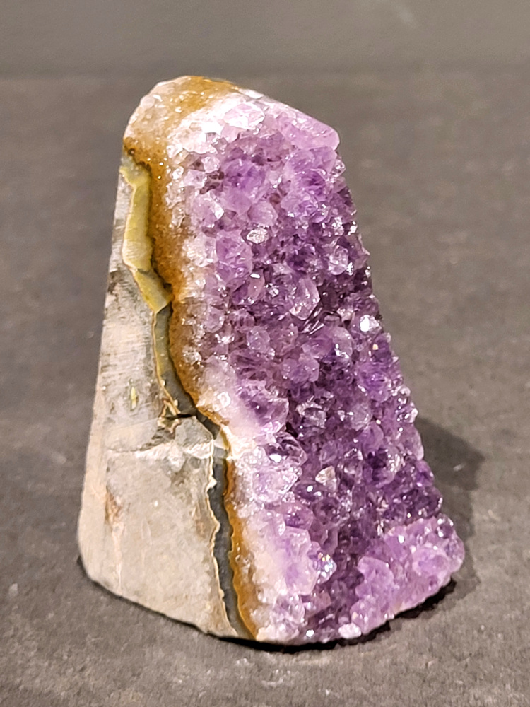 Amethist druzy, 0,2kg, 9,- euro, nr.7

Beschrijving Amethist.
Amethist is een paarse variëteit van kwarts, bekend om zijn kalmerende en spirituele eigenschappen. De kleur varieert van licht lila tot diep violet en wordt veroorzaakt door sporen van ijzer en andere elementen. Amethist wordt al eeuwenlang gewaardeerd, zowel vanwege zijn esthetische schoonheid als zijn vermeende genezende en beschermende krachten. 
Amethist is een kwartskristal, vaak te vinden in geodes (holtes in gesteente) of als afzonderlijke kristallen. 
De kleur varieert van lichtpaars tot diep violet, soms met roze of blauwe tinten. 
De kleurintensiteit kan variëren, waarbij donkerdere amethisten vaak als kwalitatief worden beschouwd. 
Soms vertoont amethist dichroïsme, waarbij je verschillende kleuren kunt zien wanneer je de steen in het licht draait. 
Vindplaatsen:
Amethist wordt gevonden in verschillende delen van de wereld, waaronder Brazilië, Uruguay, Zambia, Madagaskar, Rusland en Canada.
Het wordt vaak gevonden in bergachtige gebieden. 

Gebruik:
Amethist wordt gebruikt in sieraden, decoratieve objecten en als helende steen. 
Het wordt vaak gedragen als hanger, ring of armband, of geplaatst in ruimtes om de energie te zuiveren. 
Amethist wordt ook gebruikt in meditatie en andere spirituele praktijken. 