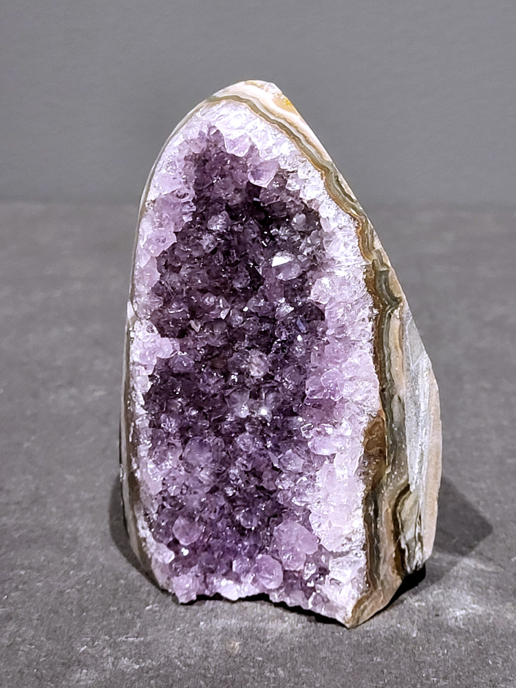 Amethist druzy, 0,2kg, 9,- euro, nr. 5

Beschrijving Amethist.
Amethist is een paarse variëteit van kwarts, bekend om zijn kalmerende en spirituele eigenschappen. De kleur varieert van licht lila tot diep violet en wordt veroorzaakt door sporen van ijzer en andere elementen. Amethist wordt al eeuwenlang gewaardeerd, zowel vanwege zijn esthetische schoonheid als zijn vermeende genezende en beschermende krachten. 
Amethist is een kwartskristal, vaak te vinden in geodes (holtes in gesteente) of als afzonderlijke kristallen. 
De kleur varieert van lichtpaars tot diep violet, soms met roze of blauwe tinten. 
De kleurintensiteit kan variëren, waarbij donkerdere amethisten vaak als kwalitatief worden beschouwd. 
Soms vertoont amethist dichroïsme, waarbij je verschillende kleuren kunt zien wanneer je de steen in het licht draait. 

Vindplaatsen:
Amethist wordt gevonden in verschillende delen van de wereld, waaronder Brazilië, Uruguay, Zambia, Madagaskar, Rusland en Canada.
Het wordt vaak gevonden in bergachtige gebieden. 

Gebruik:
Amethist wordt gebruikt in sieraden, decoratieve objecten en als helende steen. 
Het wordt vaak gedragen als hanger, ring of armband, of geplaatst in ruimtes om de energie te zuiveren. 
Amethist wordt ook gebruikt in meditatie en andere spirituele praktijken. 