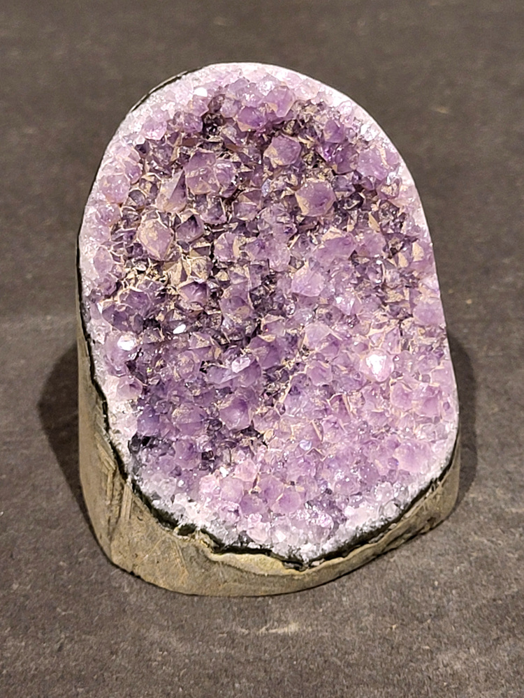 Amethist druzy, 0,3kg, 11,- euro, nr. 10

Beschrijving Amethist.
Amethist is een paarse variëteit van kwarts, bekend om zijn kalmerende en spirituele eigenschappen. De kleur varieert van licht lila tot diep violet en wordt veroorzaakt door sporen van ijzer en andere elementen. Amethist wordt al eeuwenlang gewaardeerd, zowel vanwege zijn esthetische schoonheid als zijn vermeende genezende en beschermende krachten. 
Amethist is een kwartskristal, vaak te vinden in geodes (holtes in gesteente) of als afzonderlijke kristallen. 
De kleur varieert van lichtpaars tot diep violet, soms met roze of blauwe tinten. 
De kleurintensiteit kan variëren, waarbij donkerdere amethisten vaak als kwalitatief worden beschouwd. 
Soms vertoont amethist dichroïsme, waarbij je verschillende kleuren kunt zien wanneer je de steen in het licht draait. 

Vindplaatsen:
Amethist wordt gevonden in verschillende delen van de wereld, waaronder Brazilië, Uruguay, Zambia, Madagaskar, Rusland en Canada.
Het wordt vaak gevonden in bergachtige gebieden. 

Gebruik:
Amethist wordt gebruikt in sieraden, decoratieve objecten en als helende steen. 
Het wordt vaak gedragen als hanger, ring of armband, of geplaatst in ruimtes om de energie te zuiveren. 
Amethist wordt ook gebruikt in meditatie en andere spirituele praktijken. 