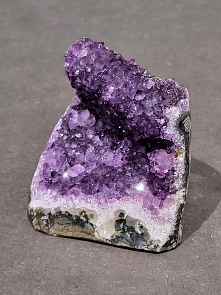 Amethist druzy, 0,4kg, 15,- euro, nr. 57

Beschrijving Amethist.
Amethist is een paarse variëteit van kwarts, bekend om zijn kalmerende en spirituele eigenschappen. De kleur varieert van licht lila tot diep violet en wordt veroorzaakt door sporen van ijzer en andere elementen. Amethist wordt al eeuwenlang gewaardeerd, zowel vanwege zijn esthetische schoonheid als zijn vermeende genezende en beschermende krachten. 
Amethist is een kwartskristal, vaak te vinden in geodes (holtes in gesteente) of als afzonderlijke kristallen. 
De kleur varieert van lichtpaars tot diep violet, soms met roze of blauwe tinten. 
De kleurintensiteit kan variëren, waarbij donkerdere amethisten vaak als kwalitatief worden beschouwd. 
Soms vertoont amethist dichroïsme, waarbij je verschillende kleuren kunt zien wanneer je de steen in het licht draait. 

Vindplaatsen:
Amethist wordt gevonden in verschillende delen van de wereld, waaronder Brazilië, Uruguay, Zambia, Madagaskar, Rusland en Canada.
Het wordt vaak gevonden in bergachtige gebieden. 

Gebruik:
Amethist wordt gebruikt in sieraden, decoratieve objecten en als helende steen. 
Het wordt vaak gedragen als hanger, ring of armband, of geplaatst in ruimtes om de energie te zuiveren. 
Amethist wordt ook gebruikt in meditatie en andere spirituele praktijken. 