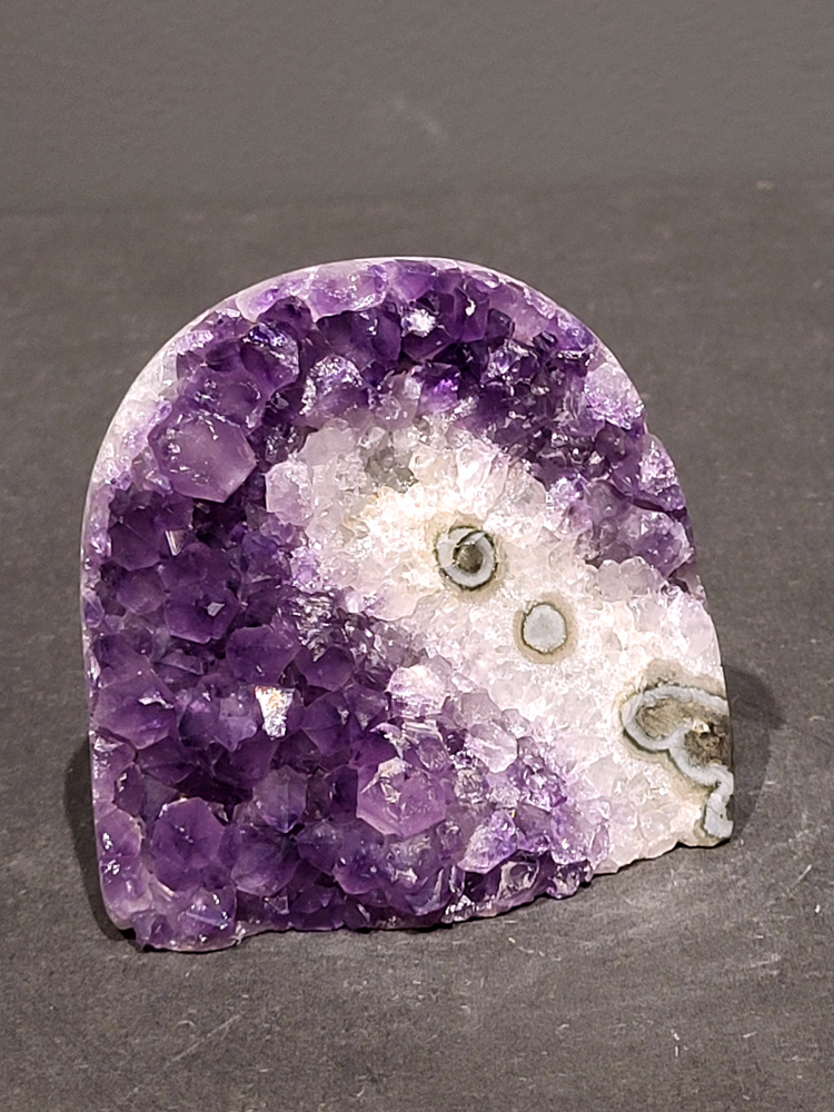Amethist druzy, 0,4kg, 17,- euro, nr. 55

Beschrijving Amethist.
Amethist is een paarse variëteit van kwarts, bekend om zijn kalmerende en spirituele eigenschappen. De kleur varieert van licht lila tot diep violet en wordt veroorzaakt door sporen van ijzer en andere elementen. Amethist wordt al eeuwenlang gewaardeerd, zowel vanwege zijn esthetische schoonheid als zijn vermeende genezende en beschermende krachten. 
Amethist is een kwartskristal, vaak te vinden in geodes (holtes in gesteente) of als afzonderlijke kristallen. 
De kleur varieert van lichtpaars tot diep violet, soms met roze of blauwe tinten. 
De kleurintensiteit kan variëren, waarbij donkerdere amethisten vaak als kwalitatief worden beschouwd. 
Soms vertoont amethist dichroïsme, waarbij je verschillende kleuren kunt zien wanneer je de steen in het licht draait. 

Vindplaatsen:
Amethist wordt gevonden in verschillende delen van de wereld, waaronder Brazilië, Uruguay, Zambia, Madagaskar, Rusland en Canada.
Het wordt vaak gevonden in bergachtige gebieden. 

Gebruik:
Amethist wordt gebruikt in sieraden, decoratieve objecten en als helende steen. 
Het wordt vaak gedragen als hanger, ring of armband, of geplaatst in ruimtes om de energie te zuiveren. 
Amethist wordt ook gebruikt in meditatie en andere spirituele praktijken. 