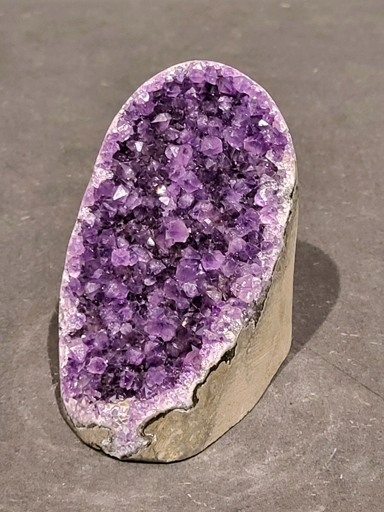 Amethist druzy, 0,4kg, 18,- euro, nr. 54

Beschrijving Amethist.
Amethist is een paarse variëteit van kwarts, bekend om zijn kalmerende en spirituele eigenschappen. De kleur varieert van licht lila tot diep violet en wordt veroorzaakt door sporen van ijzer en andere elementen. Amethist wordt al eeuwenlang gewaardeerd, zowel vanwege zijn esthetische schoonheid als zijn vermeende genezende en beschermende krachten. 
Amethist is een kwartskristal, vaak te vinden in geodes (holtes in gesteente) of als afzonderlijke kristallen. 
De kleur varieert van lichtpaars tot diep violet, soms met roze of blauwe tinten. 
De kleurintensiteit kan variëren, waarbij donkerdere amethisten vaak als kwalitatief worden beschouwd. 
Soms vertoont amethist dichroïsme, waarbij je verschillende kleuren kunt zien wanneer je de steen in het licht draait. 

Vindplaatsen:
Amethist wordt gevonden in verschillende delen van de wereld, waaronder Brazilië, Uruguay, Zambia, Madagaskar, Rusland en Canada.
Het wordt vaak gevonden in bergachtige gebieden. 

Gebruik:
Amethist wordt gebruikt in sieraden, decoratieve objecten en als helende steen. 
Het wordt vaak gedragen als hanger, ring of armband, of geplaatst in ruimtes om de energie te zuiveren. 
Amethist wordt ook gebruikt in meditatie en andere spirituele praktijken. 