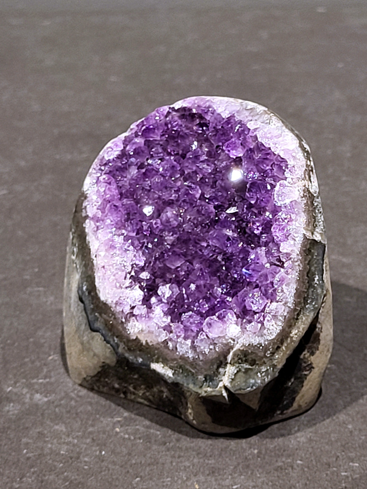 Amethist druzy, 0,5kg, 19,- euro, nr. 25

Beschrijving Amethist.
Amethist is een paarse variëteit van kwarts, bekend om zijn kalmerende en spirituele eigenschappen. De kleur varieert van licht lila tot diep violet en wordt veroorzaakt door sporen van ijzer en andere elementen. Amethist wordt al eeuwenlang gewaardeerd, zowel vanwege zijn esthetische schoonheid als zijn vermeende genezende en beschermende krachten. 
Amethist is een kwartskristal, vaak te vinden in geodes (holtes in gesteente) of als afzonderlijke kristallen. 
De kleur varieert van lichtpaars tot diep violet, soms met roze of blauwe tinten. 
De kleurintensiteit kan variëren, waarbij donkerdere amethisten vaak als kwalitatief worden beschouwd. 
Soms vertoont amethist dichroïsme, waarbij je verschillende kleuren kunt zien wanneer je de steen in het licht draait. 

Vindplaatsen:
Amethist wordt gevonden in verschillende delen van de wereld, waaronder Brazilië, Uruguay, Zambia, Madagaskar, Rusland en Canada.
Het wordt vaak gevonden in bergachtige gebieden. 

Gebruik:
Amethist wordt gebruikt in sieraden, decoratieve objecten en als helende steen. 
Het wordt vaak gedragen als hanger, ring of armband, of geplaatst in ruimtes om de energie te zuiveren. 
Amethist wordt ook gebruikt in meditatie en andere spirituele praktijken. 