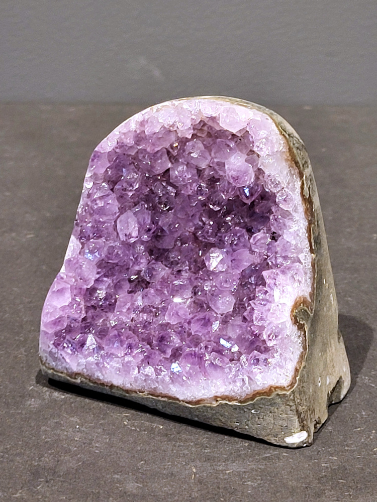 Amethist druzy, 0,5kg, 21,- euro, nr. 52

Beschrijving Amethist.
Amethist is een paarse variëteit van kwarts, bekend om zijn kalmerende en spirituele eigenschappen. De kleur varieert van licht lila tot diep violet en wordt veroorzaakt door sporen van ijzer en andere elementen. Amethist wordt al eeuwenlang gewaardeerd, zowel vanwege zijn esthetische schoonheid als zijn vermeende genezende en beschermende krachten. 
Amethist is een kwartskristal, vaak te vinden in geodes (holtes in gesteente) of als afzonderlijke kristallen. 
De kleur varieert van lichtpaars tot diep violet, soms met roze of blauwe tinten. 
De kleurintensiteit kan variëren, waarbij donkerdere amethisten vaak als kwalitatief worden beschouwd. 
Soms vertoont amethist dichroïsme, waarbij je verschillende kleuren kunt zien wanneer je de steen in het licht draait. 

Vindplaatsen:
Amethist wordt gevonden in verschillende delen van de wereld, waaronder Brazilië, Uruguay, Zambia, Madagaskar, Rusland en Canada.
Het wordt vaak gevonden in bergachtige gebieden. 

Gebruik:
Amethist wordt gebruikt in sieraden, decoratieve objecten en als helende steen. 
Het wordt vaak gedragen als hanger, ring of armband, of geplaatst in ruimtes om de energie te zuiveren. 
Amethist wordt ook gebruikt in meditatie en andere spirituele praktijken. 