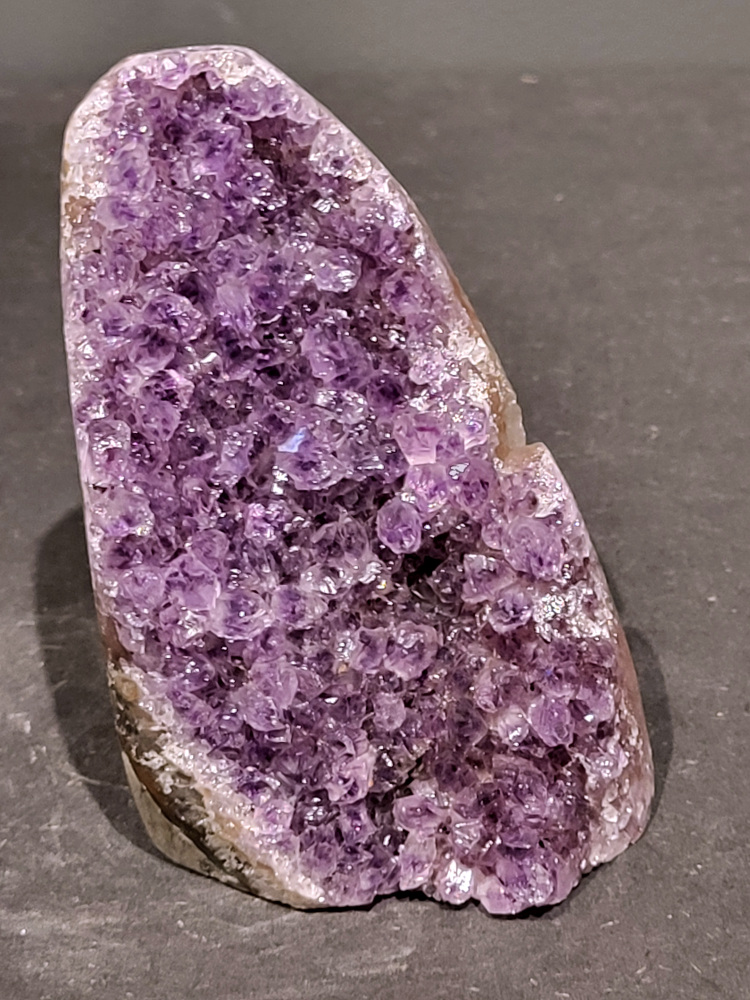 Amethist druzy, 0,8kg, 30,- euro, nr. 47

Beschrijving Amethist.
Amethist is een paarse variëteit van kwarts, bekend om zijn kalmerende en spirituele eigenschappen. De kleur varieert van licht lila tot diep violet en wordt veroorzaakt door sporen van ijzer en andere elementen. Amethist wordt al eeuwenlang gewaardeerd, zowel vanwege zijn esthetische schoonheid als zijn vermeende genezende en beschermende krachten. 
Amethist is een kwartskristal, vaak te vinden in geodes (holtes in gesteente) of als afzonderlijke kristallen. 
De kleur varieert van lichtpaars tot diep violet, soms met roze of blauwe tinten. 
De kleurintensiteit kan variëren, waarbij donkerdere amethisten vaak als kwalitatief worden beschouwd. 
Soms vertoont amethist dichroïsme, waarbij je verschillende kleuren kunt zien wanneer je de steen in het licht draait. 

Vindplaatsen:
Amethist wordt gevonden in verschillende delen van de wereld, waaronder Brazilië, Uruguay, Zambia, Madagaskar, Rusland en Canada.
Het wordt vaak gevonden in bergachtige gebieden. 

Gebruik:
Amethist wordt gebruikt in sieraden, decoratieve objecten en als helende steen. 
Het wordt vaak gedragen als hanger, ring of armband, of geplaatst in ruimtes om de energie te zuiveren. 
Amethist wordt ook gebruikt in meditatie en andere spirituele praktijken. 
