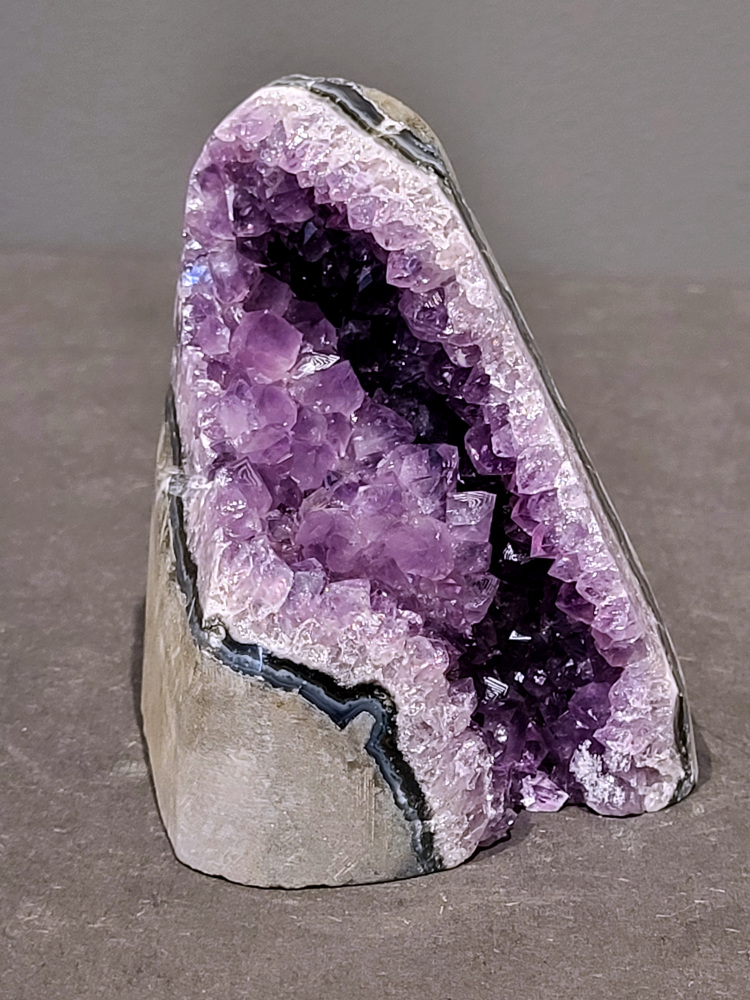 Amethist druzy, 0,8kg, 31,- euro, nr. 40

Beschrijving Amethist.
Amethist is een paarse variëteit van kwarts, bekend om zijn kalmerende en spirituele eigenschappen. De kleur varieert van licht lila tot diep violet en wordt veroorzaakt door sporen van ijzer en andere elementen. Amethist wordt al eeuwenlang gewaardeerd, zowel vanwege zijn esthetische schoonheid als zijn vermeende genezende en beschermende krachten. 
Amethist is een kwartskristal, vaak te vinden in geodes (holtes in gesteente) of als afzonderlijke kristallen. 
De kleur varieert van lichtpaars tot diep violet, soms met roze of blauwe tinten. 
De kleurintensiteit kan variëren, waarbij donkerdere amethisten vaak als kwalitatief worden beschouwd. 
Soms vertoont amethist dichroïsme, waarbij je verschillende kleuren kunt zien wanneer je de steen in het licht draait. 

Vindplaatsen:
Amethist wordt gevonden in verschillende delen van de wereld, waaronder Brazilië, Uruguay, Zambia, Madagaskar, Rusland en Canada.
Het wordt vaak gevonden in bergachtige gebieden. 

Gebruik:
Amethist wordt gebruikt in sieraden, decoratieve objecten en als helende steen. 
Het wordt vaak gedragen als hanger, ring of armband, of geplaatst in ruimtes om de energie te zuiveren. 
Amethist wordt ook gebruikt in meditatie en andere spirituele praktijken. 