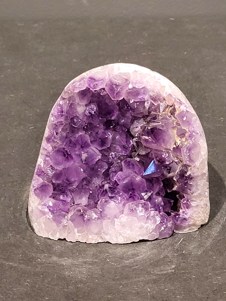Amethist druzy, 0,8kg, 34,-euro nr.45

Beschrijving Amethist.
Amethist is een paarse variëteit van kwarts, bekend om zijn kalmerende en spirituele eigenschappen. De kleur varieert van licht lila tot diep violet en wordt veroorzaakt door sporen van ijzer en andere elementen. Amethist wordt al eeuwenlang gewaardeerd, zowel vanwege zijn esthetische schoonheid als zijn vermeende genezende en beschermende krachten. 
Amethist is een kwartskristal, vaak te vinden in geodes (holtes in gesteente) of als afzonderlijke kristallen. 
De kleur varieert van lichtpaars tot diep violet, soms met roze of blauwe tinten. 
De kleurintensiteit kan variëren, waarbij donkerdere amethisten vaak als kwalitatief worden beschouwd. 
Soms vertoont amethist dichroïsme, waarbij je verschillende kleuren kunt zien wanneer je de steen in het licht draait. 

Vindplaatsen:
Amethist wordt gevonden in verschillende delen van de wereld, waaronder Brazilië, Uruguay, Zambia, Madagaskar, Rusland en Canada.
Het wordt vaak gevonden in bergachtige gebieden. 

Gebruik:
Amethist wordt gebruikt in sieraden, decoratieve objecten en als helende steen. 
Het wordt vaak gedragen als hanger, ring of armband, of geplaatst in ruimtes om de energie te zuiveren. 
Amethist wordt ook gebruikt in meditatie en andere spirituele praktijken. 