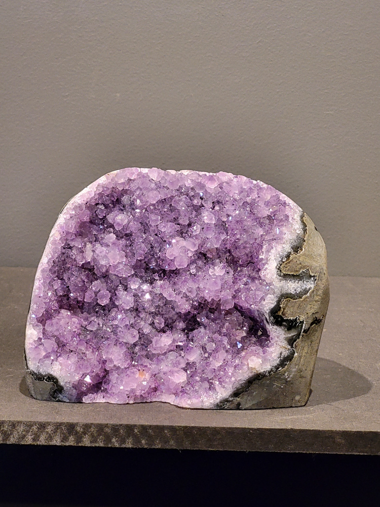 Amethist druzy, 1,1kg, 45,- euro, nr. 35

Beschrijving Amethist.
Amethist is een paarse variëteit van kwarts, bekend om zijn kalmerende en spirituele eigenschappen. De kleur varieert van licht lila tot diep violet en wordt veroorzaakt door sporen van ijzer en andere elementen. Amethist wordt al eeuwenlang gewaardeerd, zowel vanwege zijn esthetische schoonheid als zijn vermeende genezende en beschermende krachten. 
Amethist is een kwartskristal, vaak te vinden in geodes (holtes in gesteente) of als afzonderlijke kristallen. 
De kleur varieert van lichtpaars tot diep violet, soms met roze of blauwe tinten. 
De kleurintensiteit kan variëren, waarbij donkerdere amethisten vaak als kwalitatief worden beschouwd. 
Soms vertoont amethist dichroïsme, waarbij je verschillende kleuren kunt zien wanneer je de steen in het licht draait. 

Vindplaatsen:
Amethist wordt gevonden in verschillende delen van de wereld, waaronder Brazilië, Uruguay, Zambia, Madagaskar, Rusland en Canada.
Het wordt vaak gevonden in bergachtige gebieden. 

Gebruik:
Amethist wordt gebruikt in sieraden, decoratieve objecten en als helende steen. 
Het wordt vaak gedragen als hanger, ring of armband, of geplaatst in ruimtes om de energie te zuiveren. 
Amethist wordt ook gebruikt in meditatie en andere spirituele praktijken. 